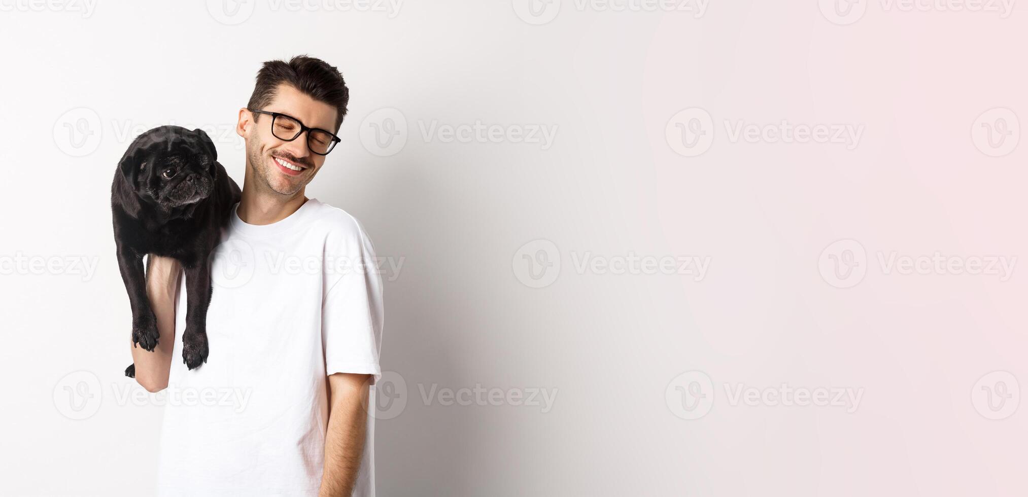Happy man in love with dog, holding puppy on shoulder and smiling, standing over white background photo