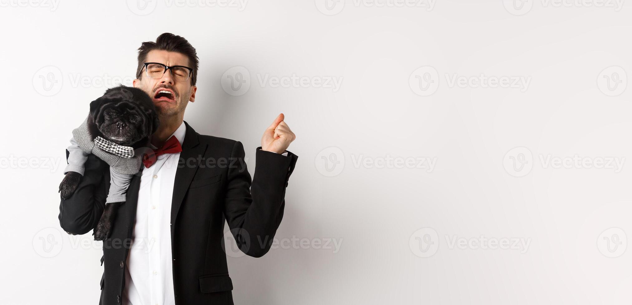 Sad man in suit, holding cute small dog on shoulder and crying with disappointed face, standing distressed over white background photo