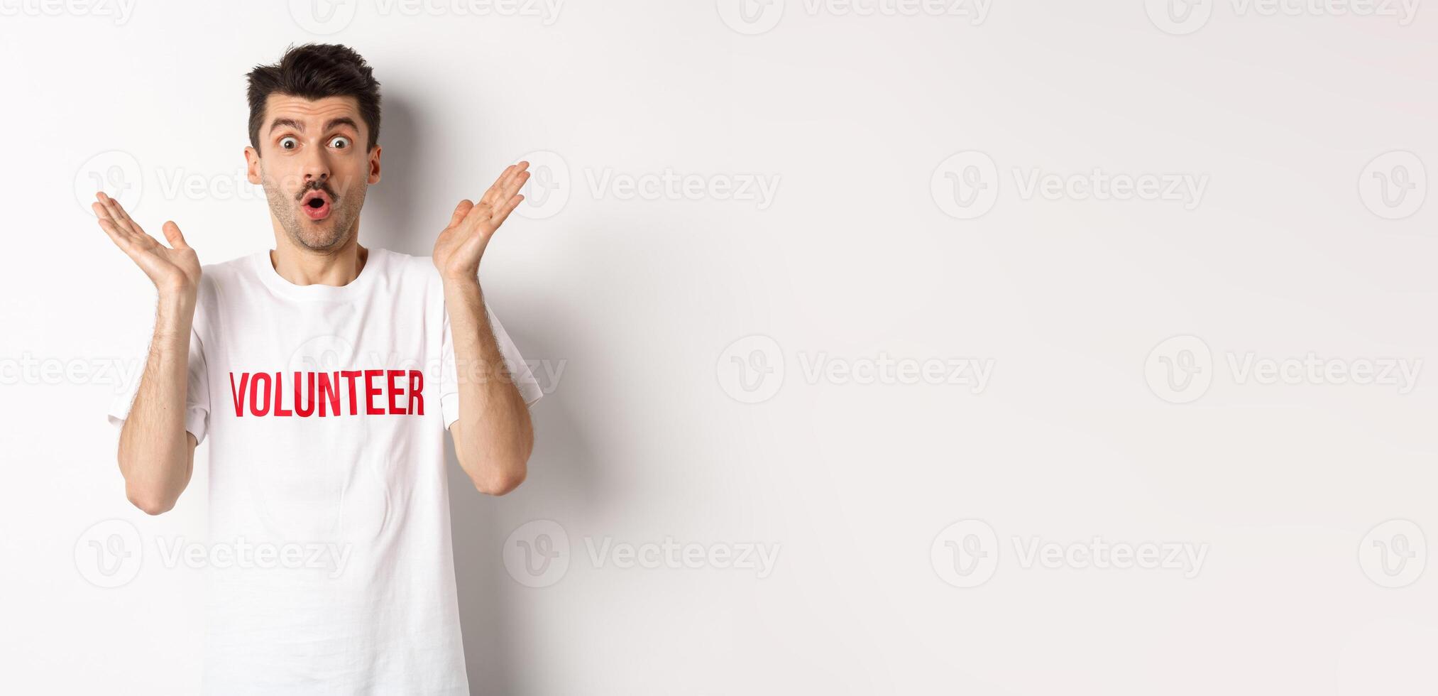 Amazed male volunteer in white t-shirt hear great news, clap hands and staring at camera surprised, posing over studio background photo