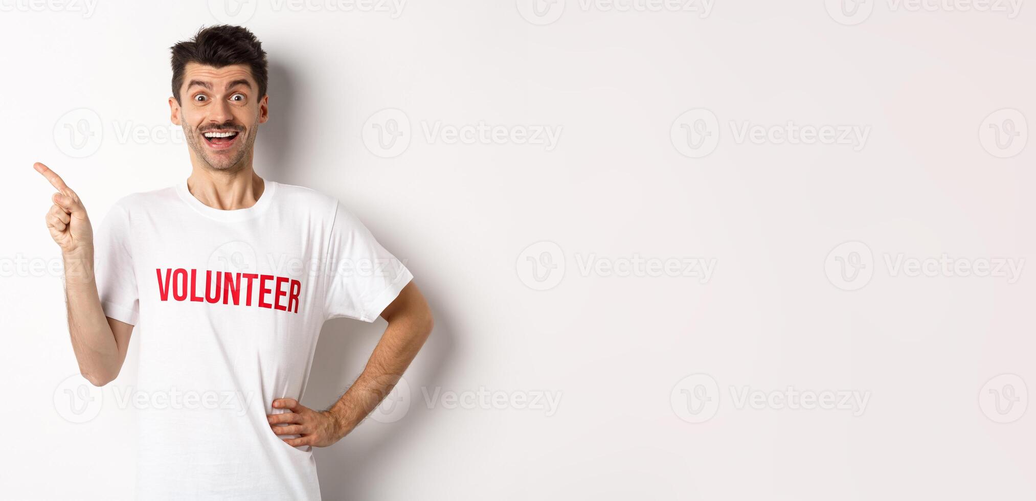 Happy smiling volunteer pointing finger left at copy space, showing announcement, white background photo