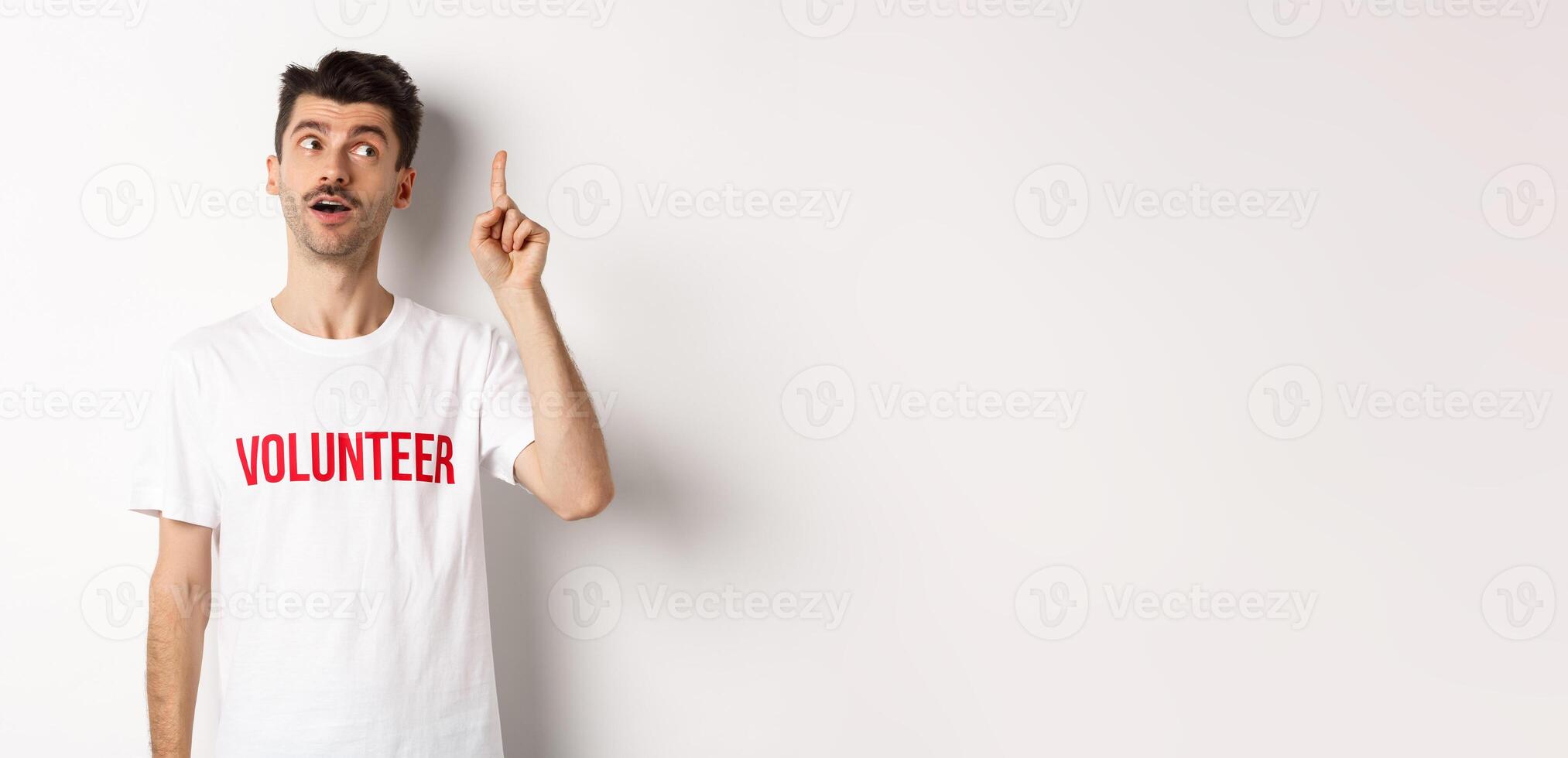 Handsome young man in volunteer t-shirt having an idea, raising finger and saying suggestion, white background photo