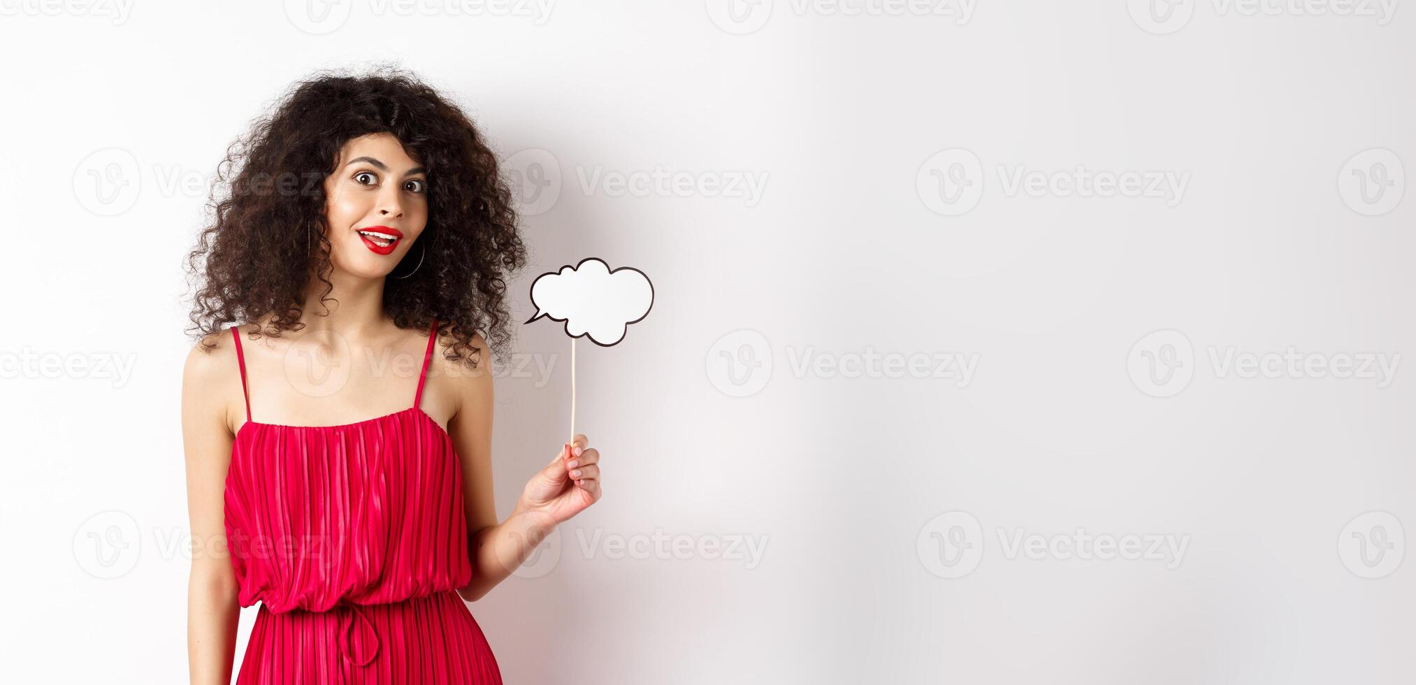 Beautiful woman with curly hair, wearing red dress, holding comment cloud, say something, standing on white background photo