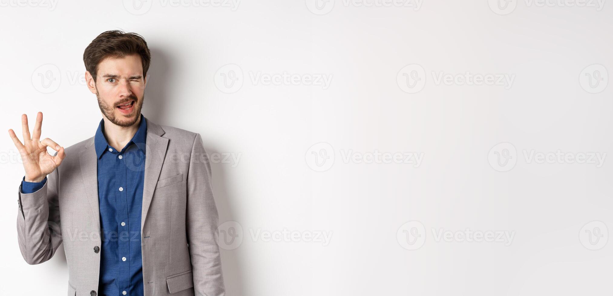 All good. Confident male ceo manager showing okay sign and winking, everything under control, praising nice work, standing on white background photo
