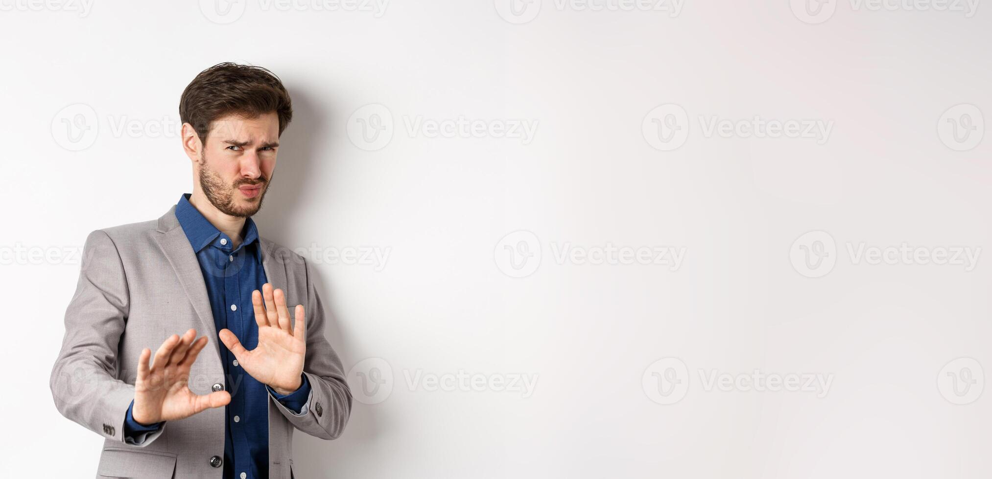 Stay away. Reluctant businessman step back with concerned disgusted face, raising hands to block bad offer, rejecting something awful, telling no and decline proposal, white background photo