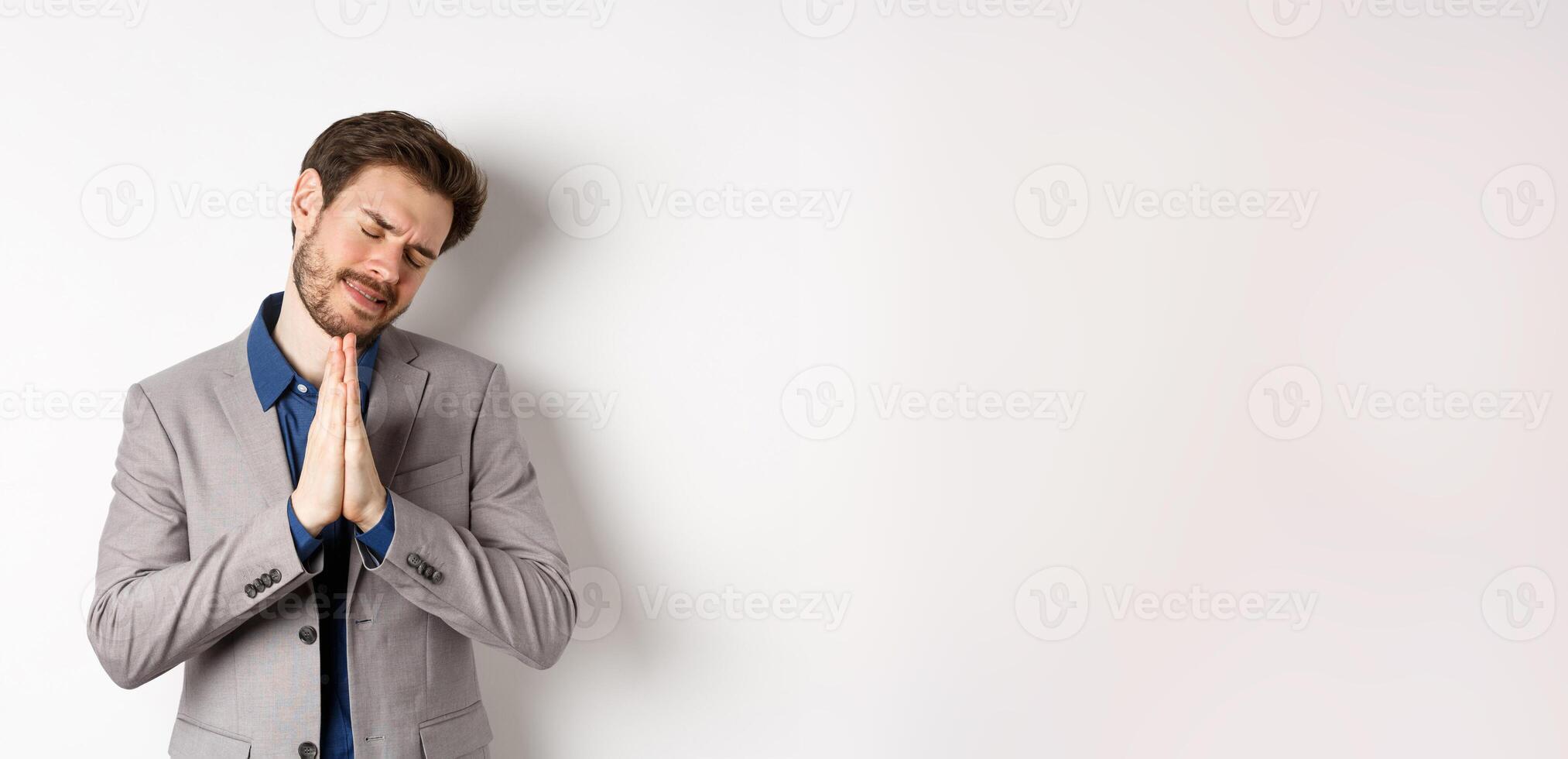 Pleading businessman begging for help, holding hands in pray and asking for favour, need something, say please, standing on white background photo