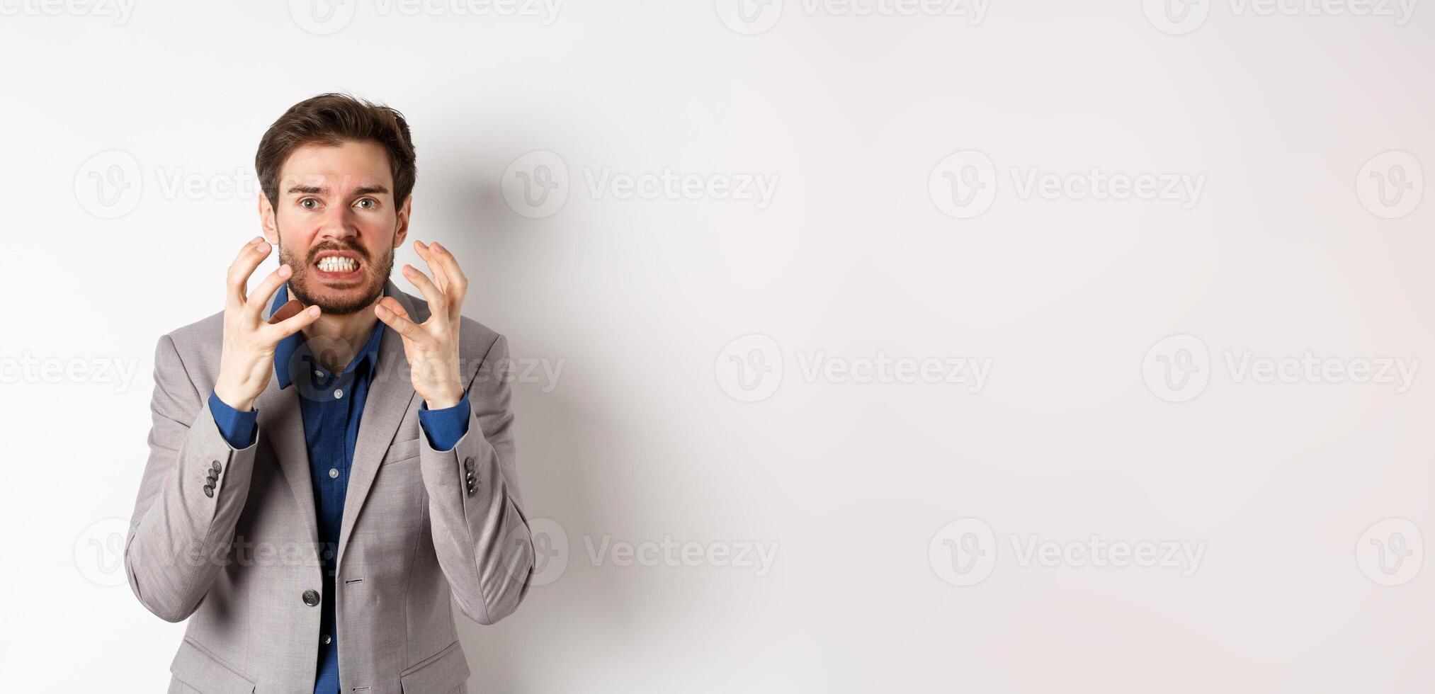 Angry and annoyed businessman wants to kill someone, clenching hands and teeth, looking mad at camera, going to strangle person, standing on white background photo