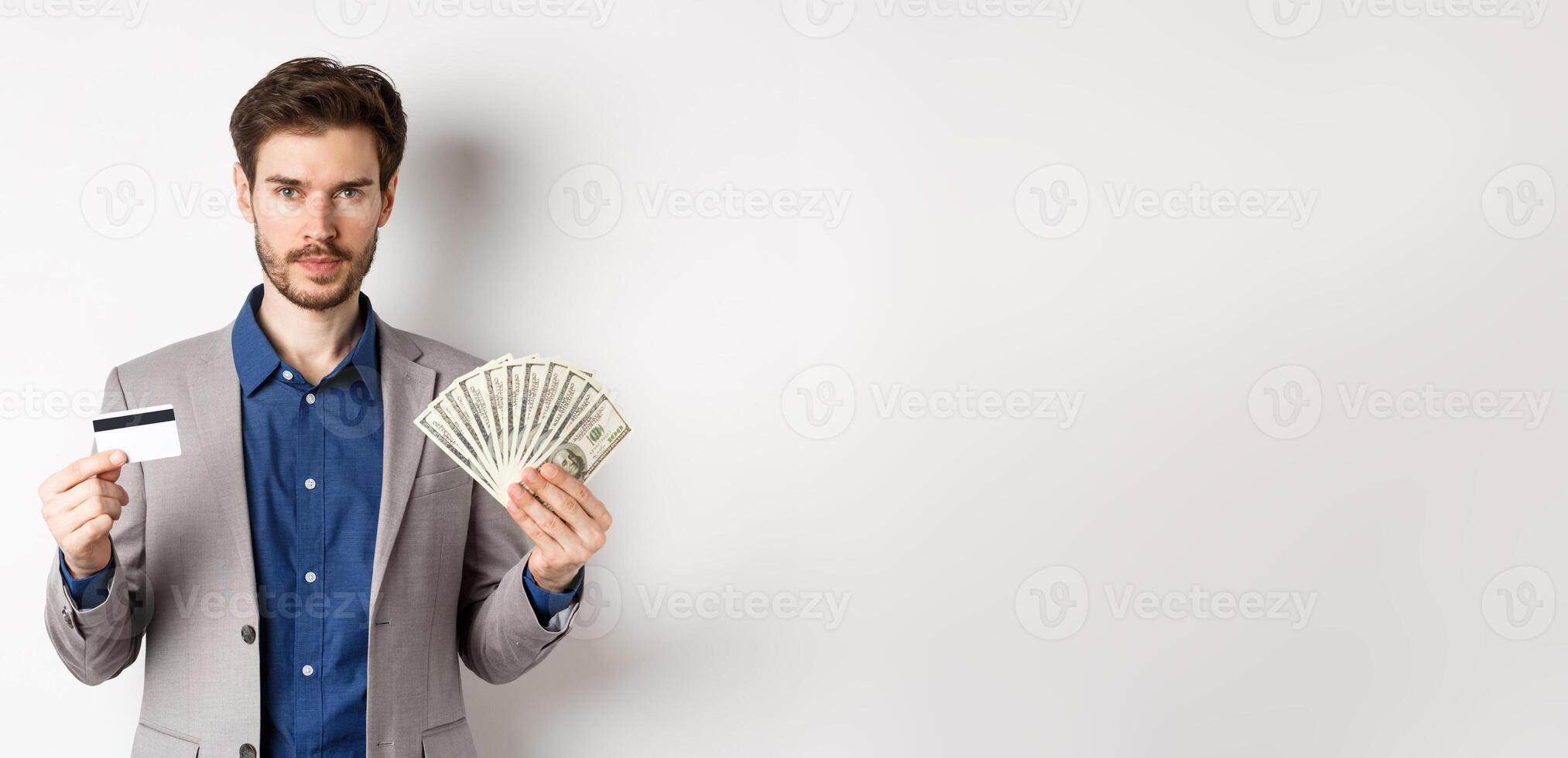 Successful businessman making money, standing in suit with dollar bills and plastic credit card, white background photo