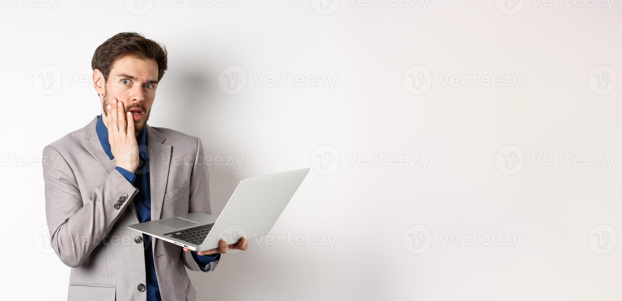 Shocked and troubled businessman have trouble on laptop, looking worried at camera, made mistake at work, standing on white background in suit photo