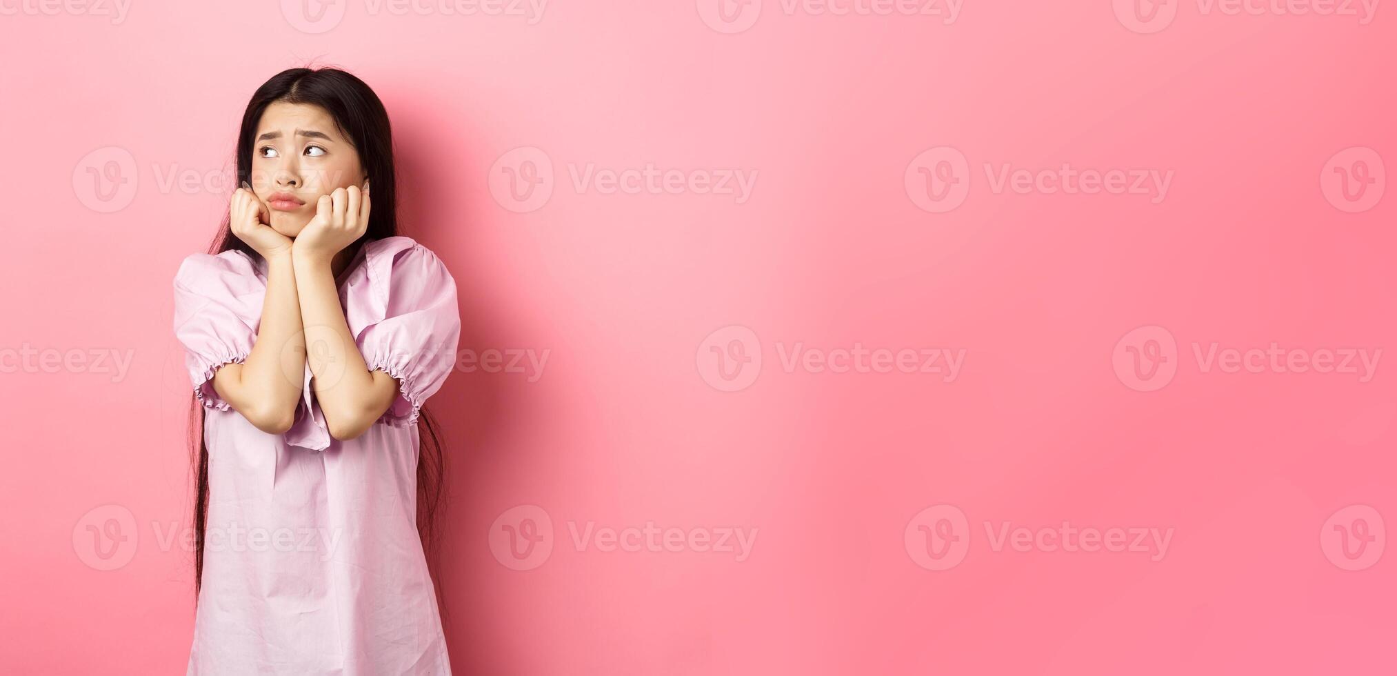 Sad and lonely asian girl look left and frowning, standing distressed against pink background photo