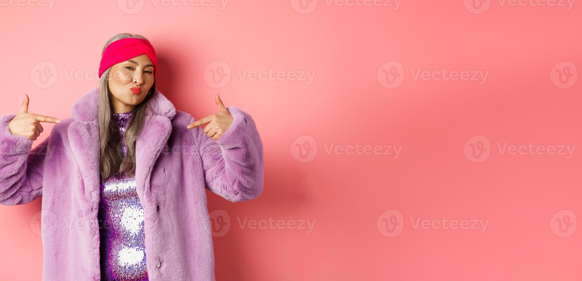 Fashion and shopping concept. Cool and stylish asian senior woman pointing fingers at herself and her trendy outfit, pucker lips and looking confident at camera, check this out gesture photo