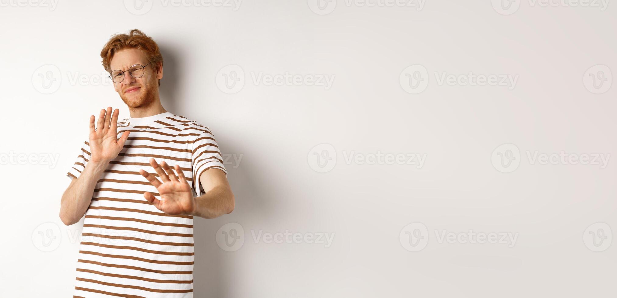 Displeased young man with red hair and bristle showing stop gesture, refusing something bad with disgusted face, standing over white background photo