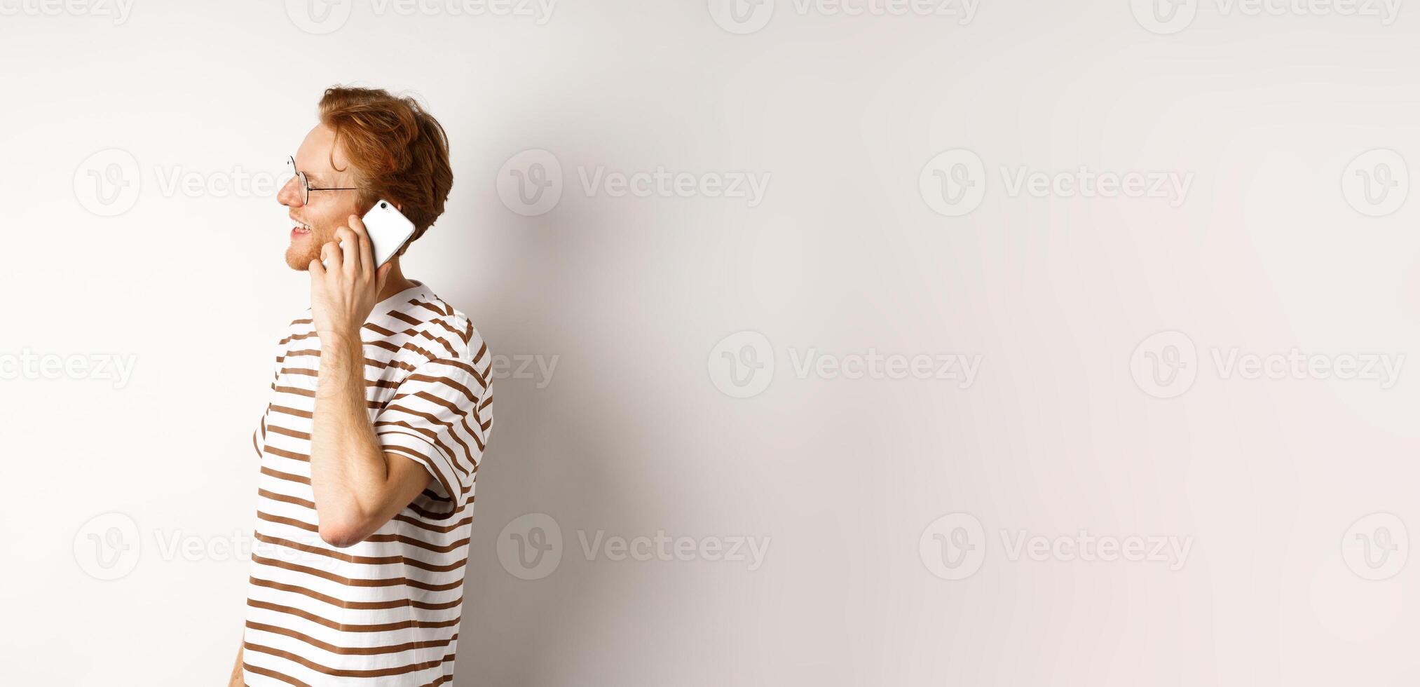 Profile of happy young handsome man talking on mobile phone, looking left and smiling, standing over white background photo