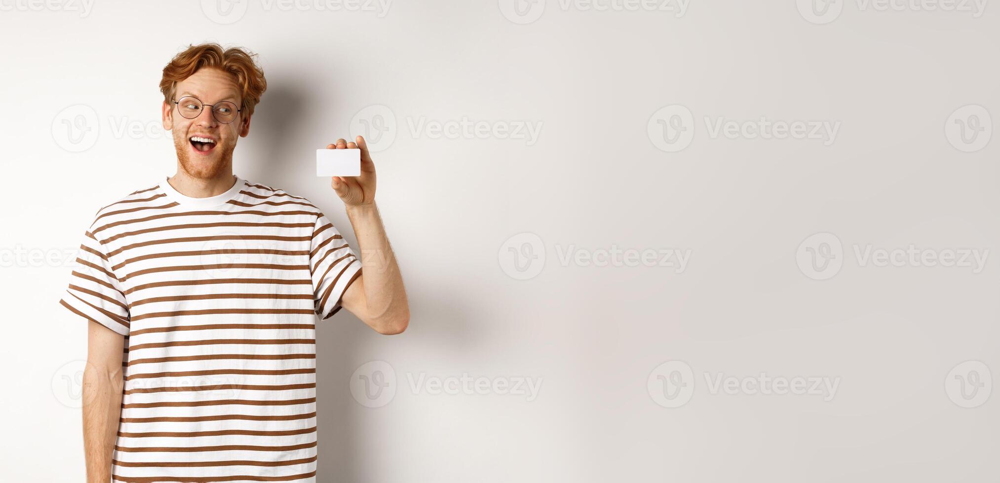 Shopping and finance concept. Amazed caucasian redhead man showing plastic card, saying wow and staring impressed at camera, white background photo