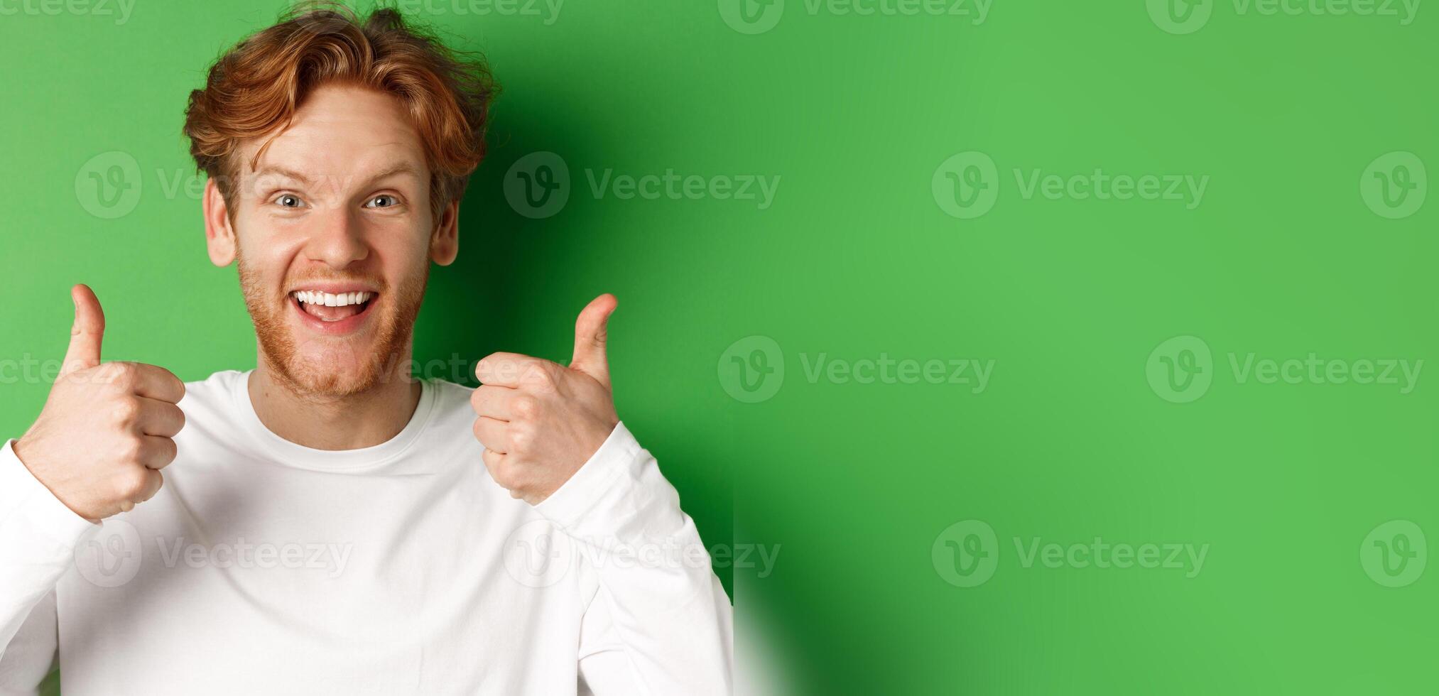 Emotions and fashion concept. Close up of cheerful redhead man showing thumbs-up and say yes, approve and like something cool, green background photo