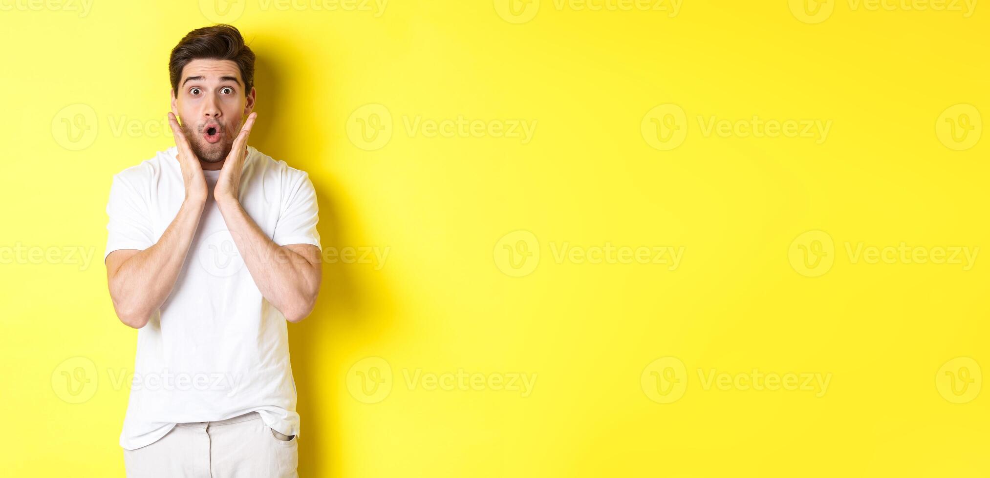 Image of handsome man looking surprised, gasping and saying wow, looking at promo offer amazed, standing over yellow background photo