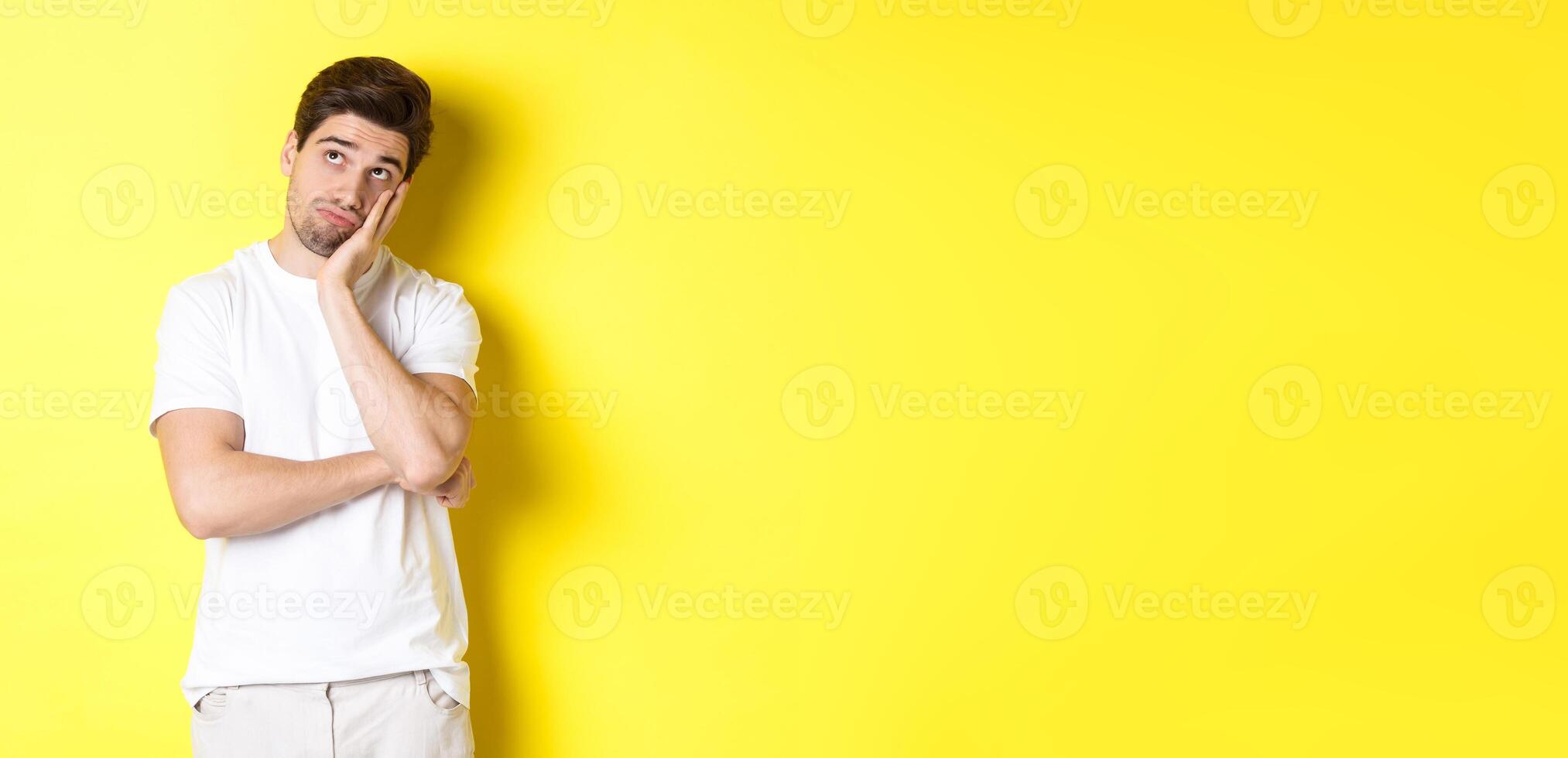 Bored and gloomy guy looking up, imaging things, standing over yellow background photo