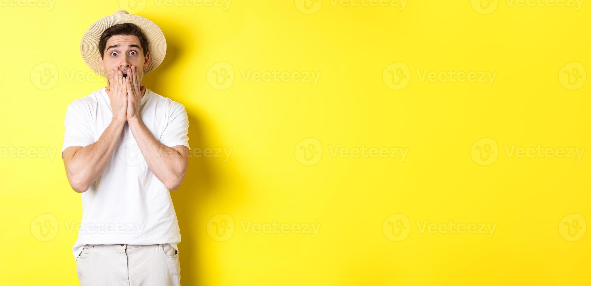 Concept of tourism and summer. Shocked guy jumping from fear, standing startled against yellow background photo