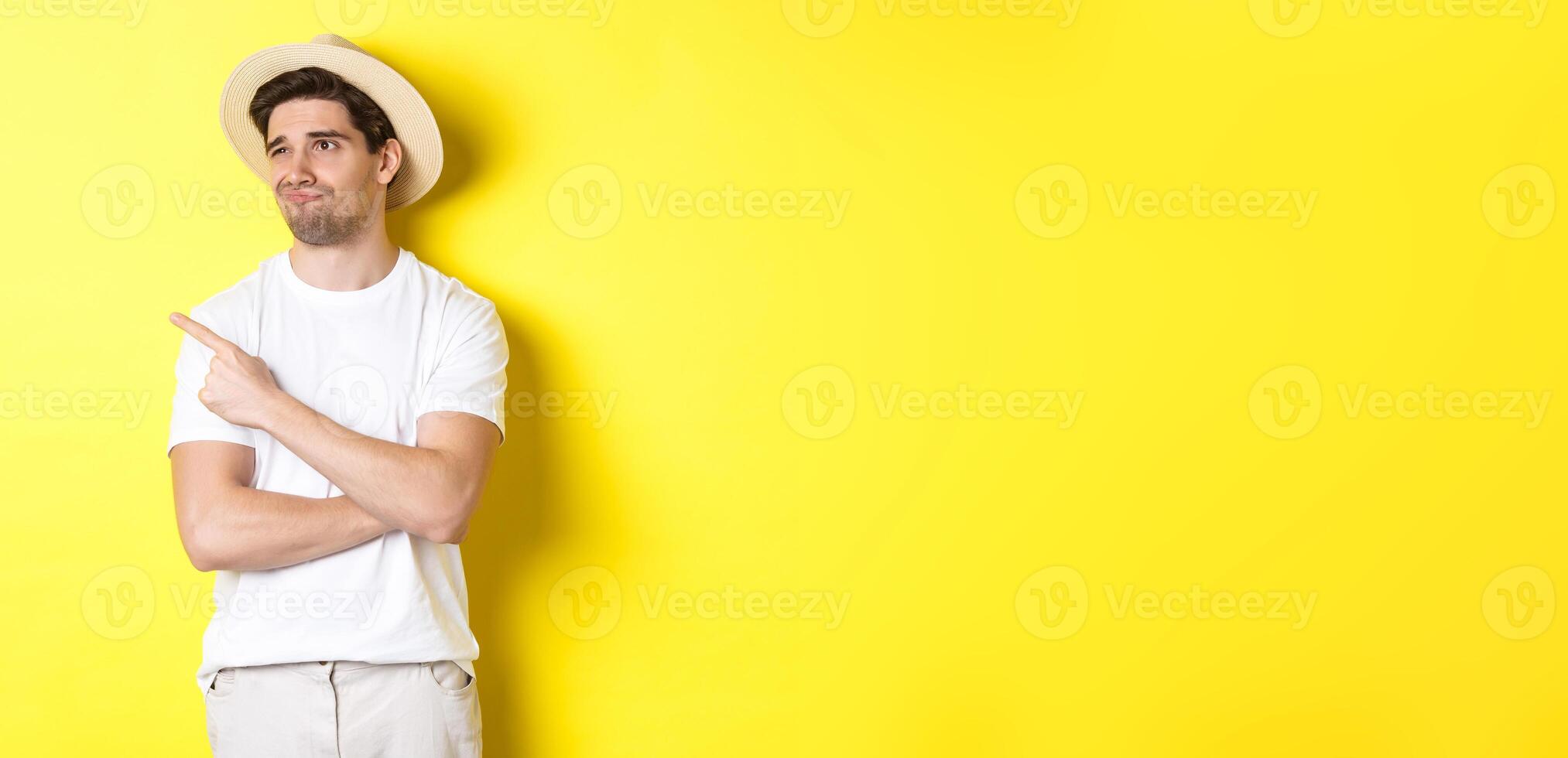 Concept of tourism and lifestyle. Displeased male tourist complaining, looking and pointing finger at upper left corner promo with disappointment, standing against yellow background photo