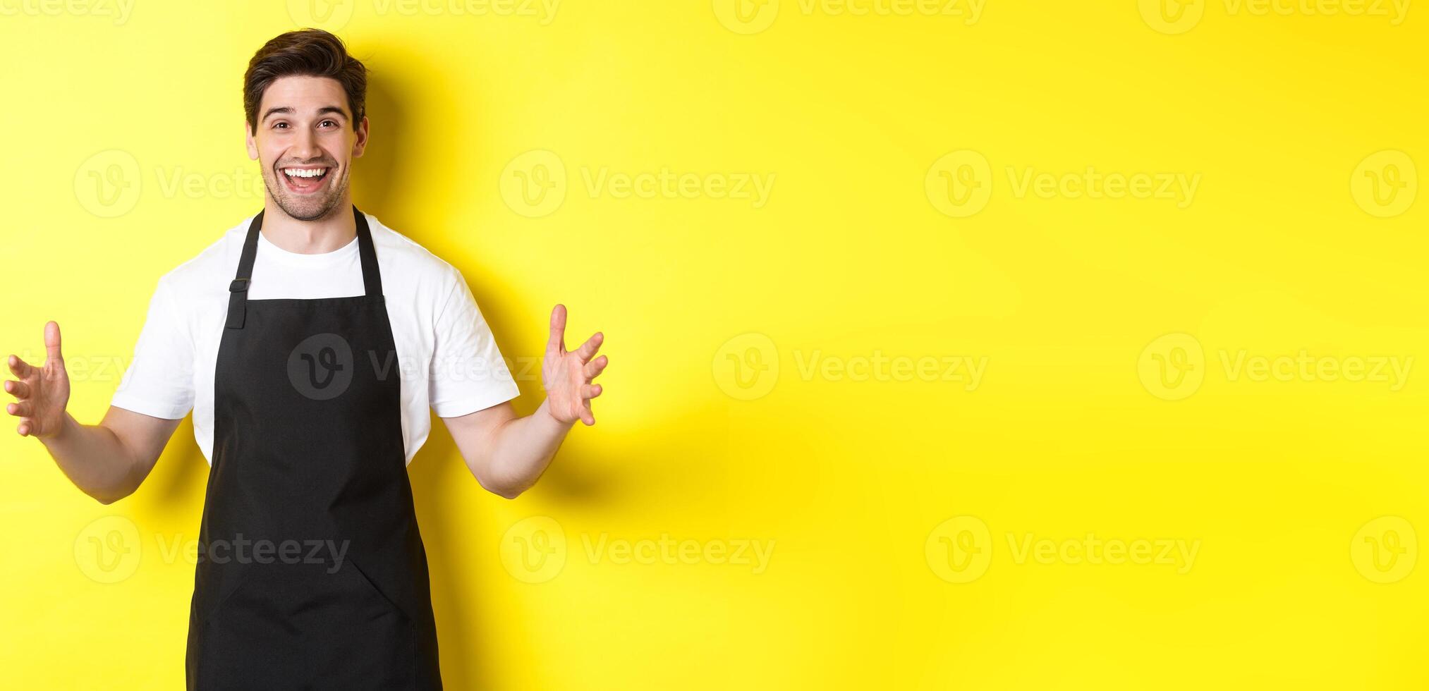 Happy barista holding something big, shaping large object, standing over yellow background photo