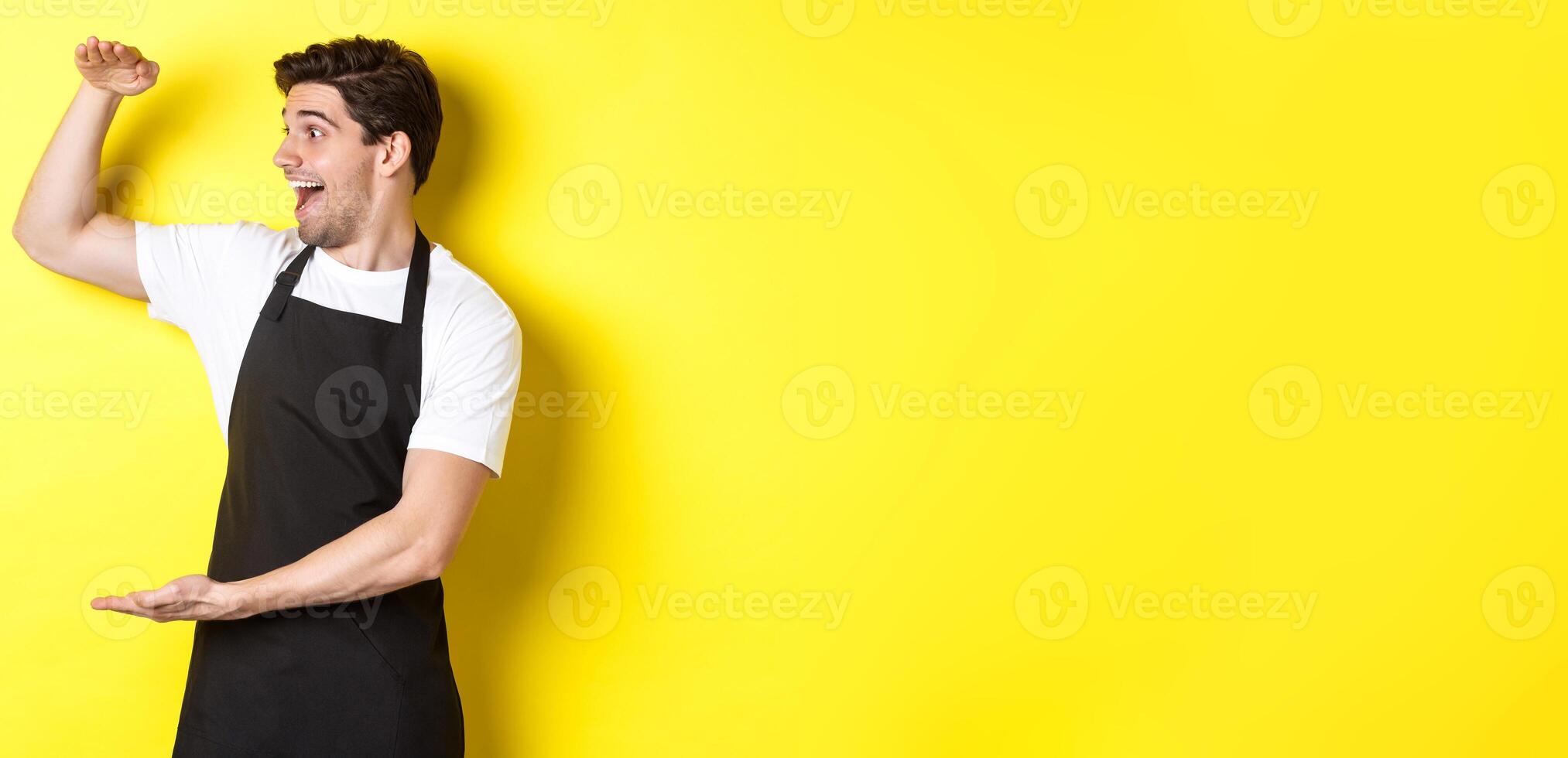 Man looking surprised at something large, standing in black apron against yellow background photo