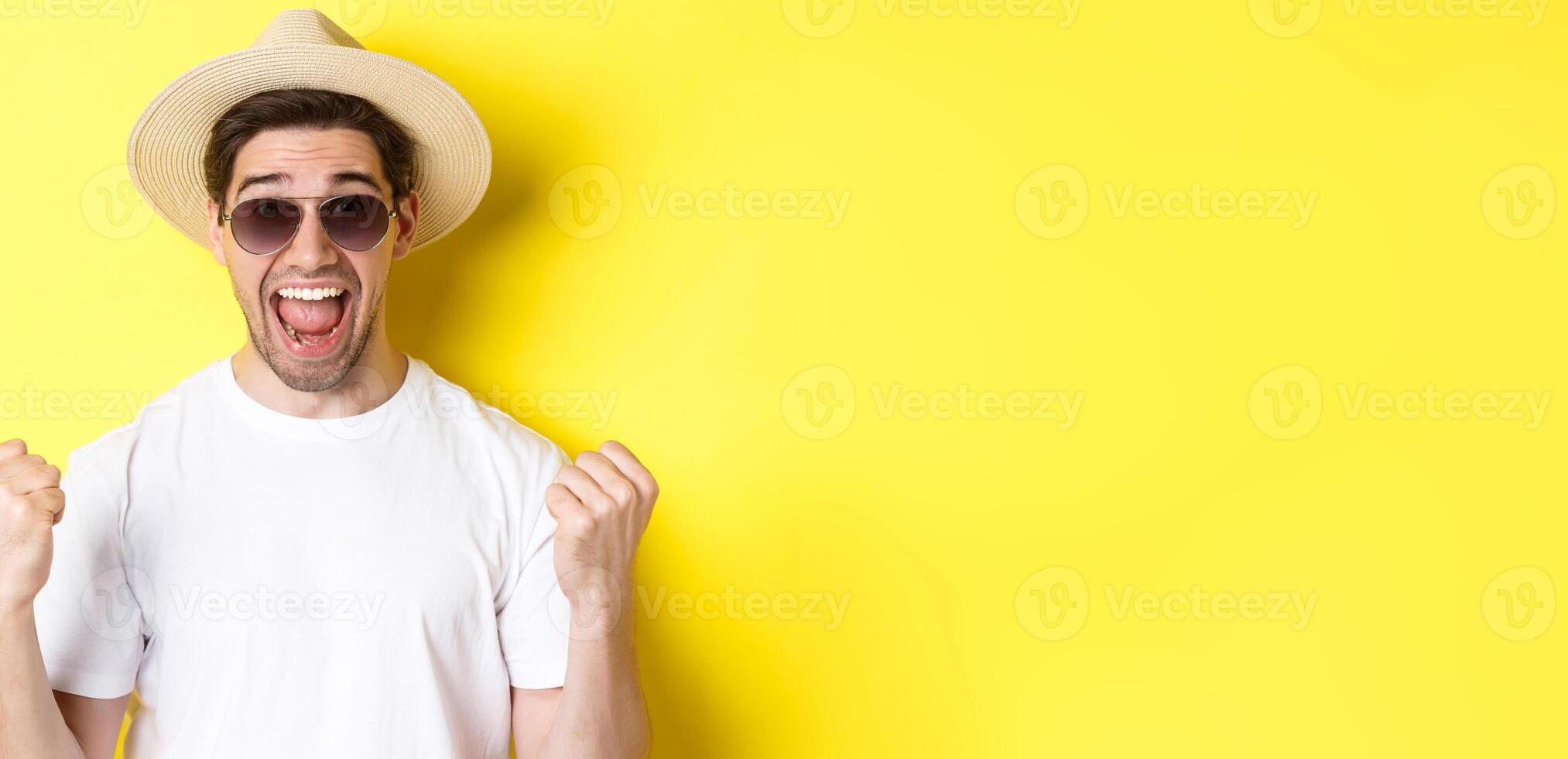 Concept of tourism and holidays. Lucky man tourist winning tickets, making fist pump and saying yes, wearing vacation clothes, standing over yellow background photo