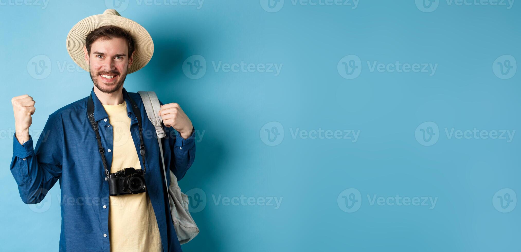 Happy tourist enjoying summer vacation, smiling and saying yes with fist pump, celebrating on holidays, feeling joy as finaly travel abroad, standing on blue background photo