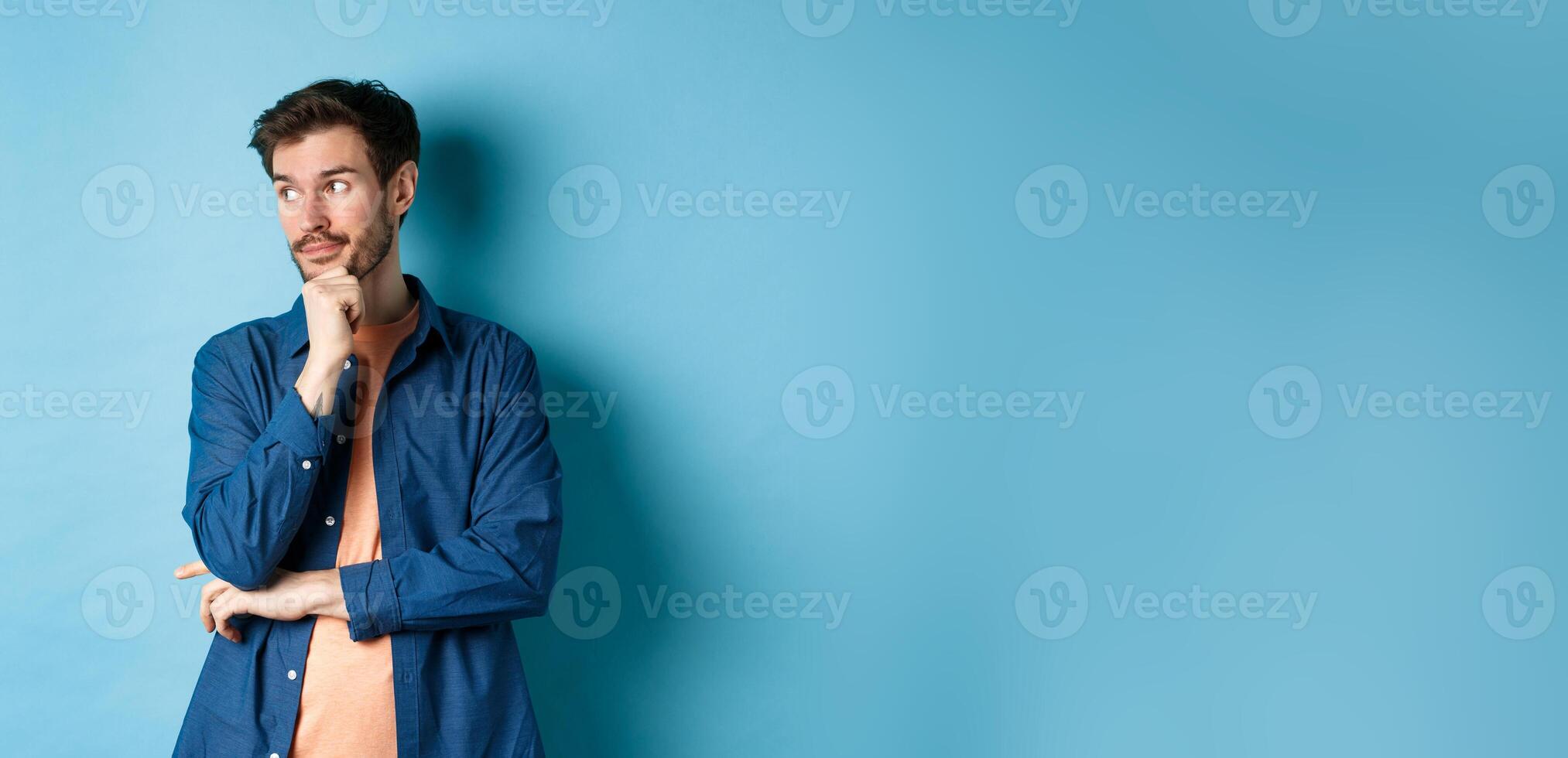 Thoughtful caucasian man looking aside at empty space and thinking, standing pensive on blue background photo