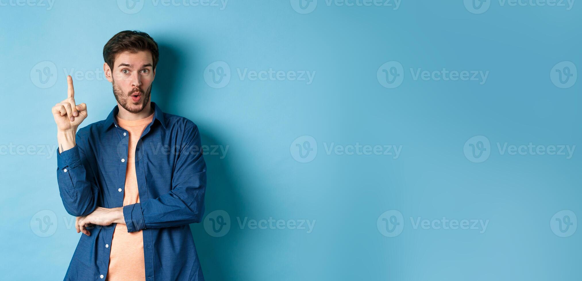 Handsome young man having an idea, pitching plan, raising finger and saying suggestion, standing on blue background photo