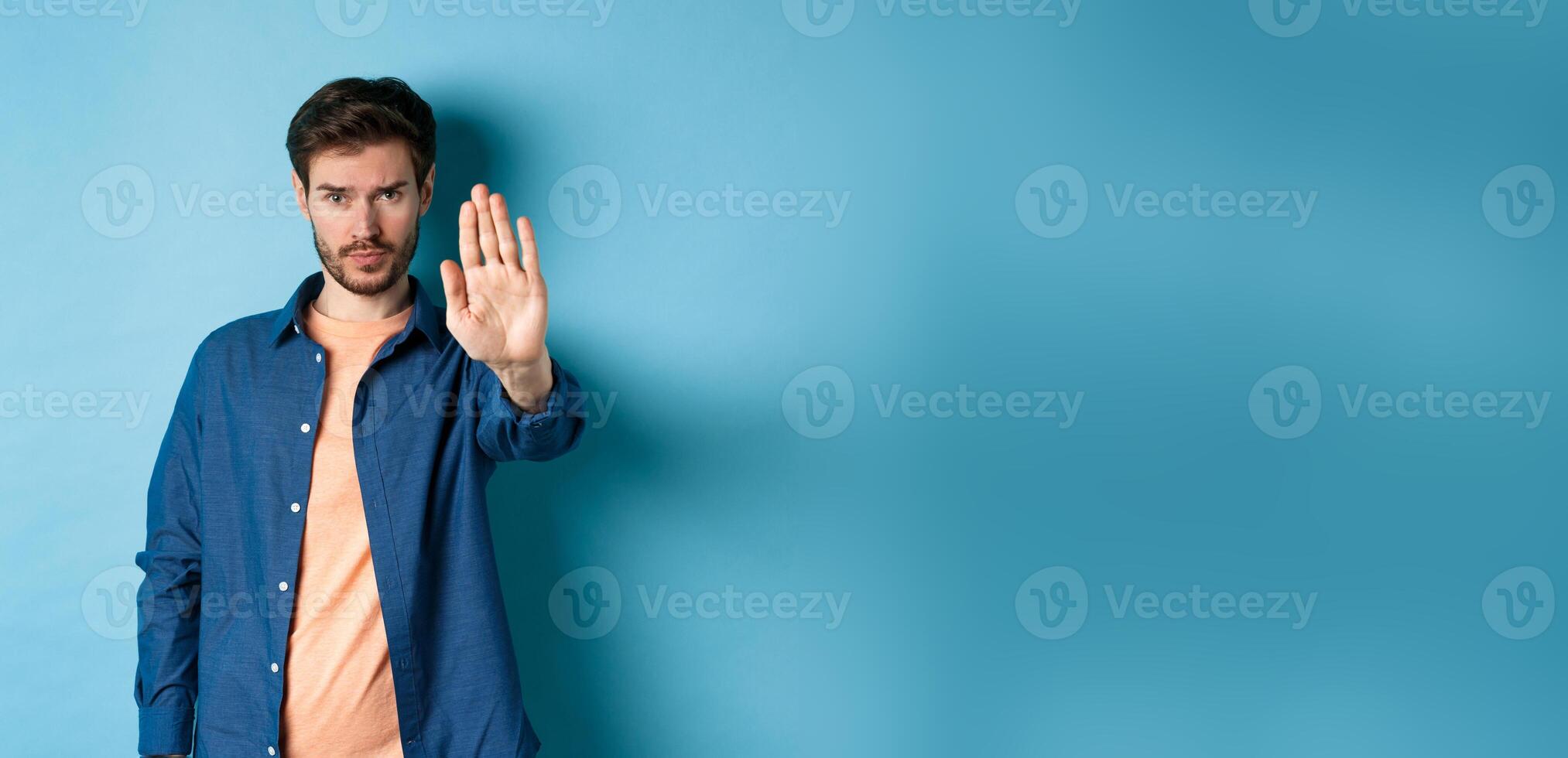 Upset man frowning and asking to stop, stretch out hand to prohibit or disagree with something bad, standing on blue background photo