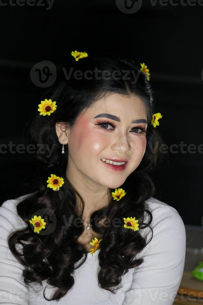 Beauty portrait of a cheerful young indonesia woman in the studio from Korean Japanese makeup concept with flower decoration in the hair area, beautiful face, glowing white skin on a black background photo