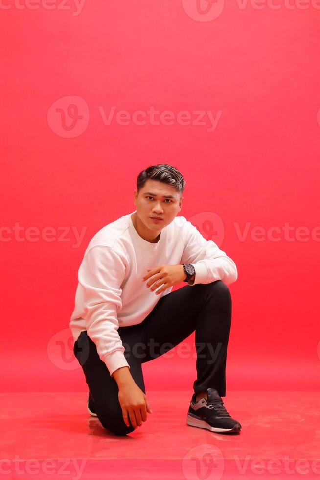 The entire body of an adult Asian man wearing an elegant white sweater squats and holds his knees. for fashion content, advertising, business photo