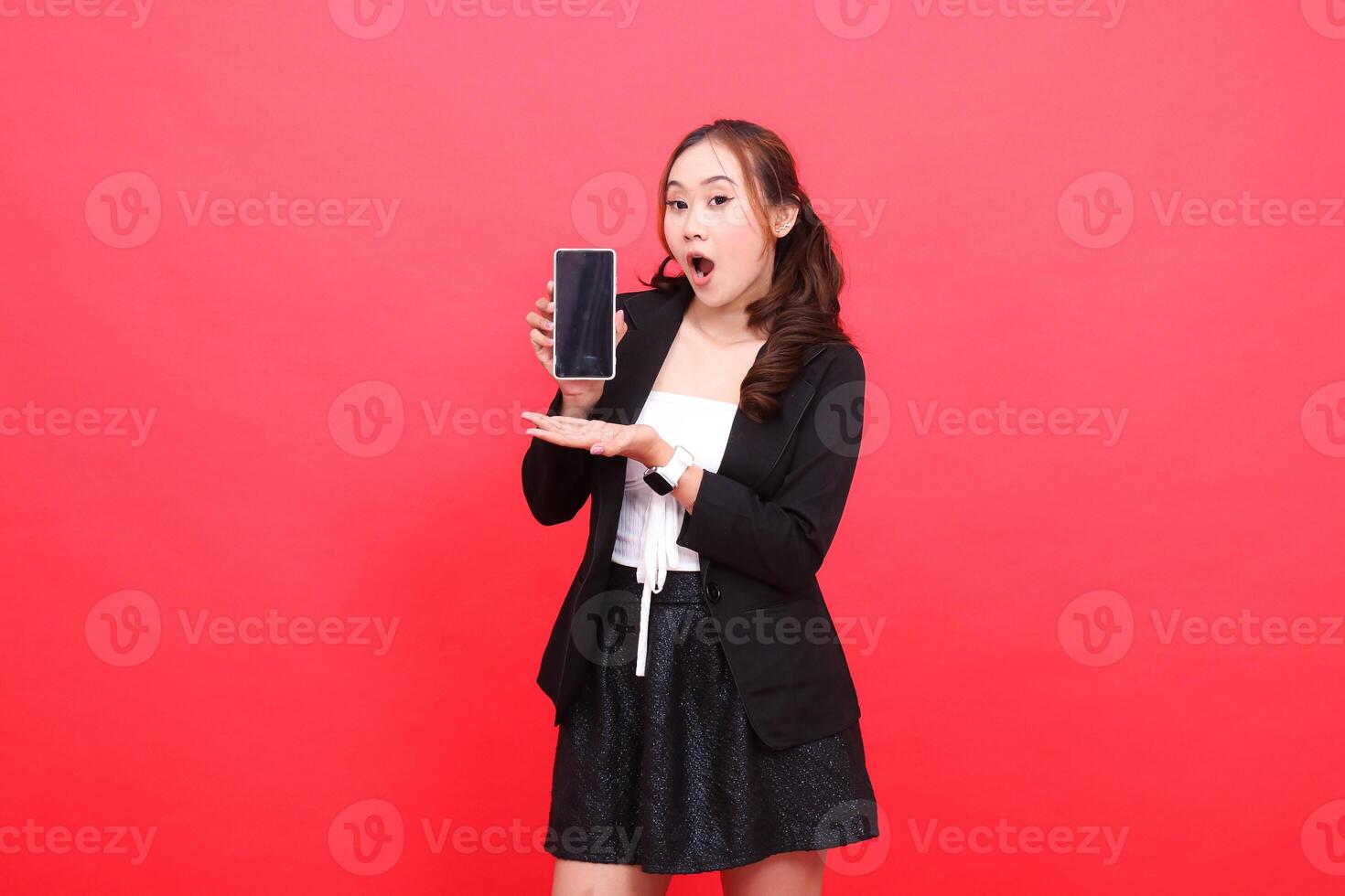 expression of young Asian career girl shocked at the camera wearing a black formal suit holding a smartphone while introducing, for technology, business, advertising, financial content photo