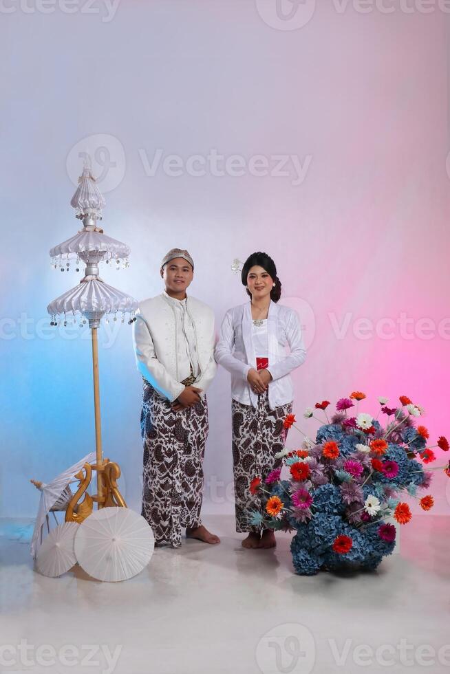 full body length of a pair of smiling Asian boy and girl wearing traditional Javanese traditional clothes, white velvet bridal kebaya, pre-wedding concept on a white studio background. for advertising photo
