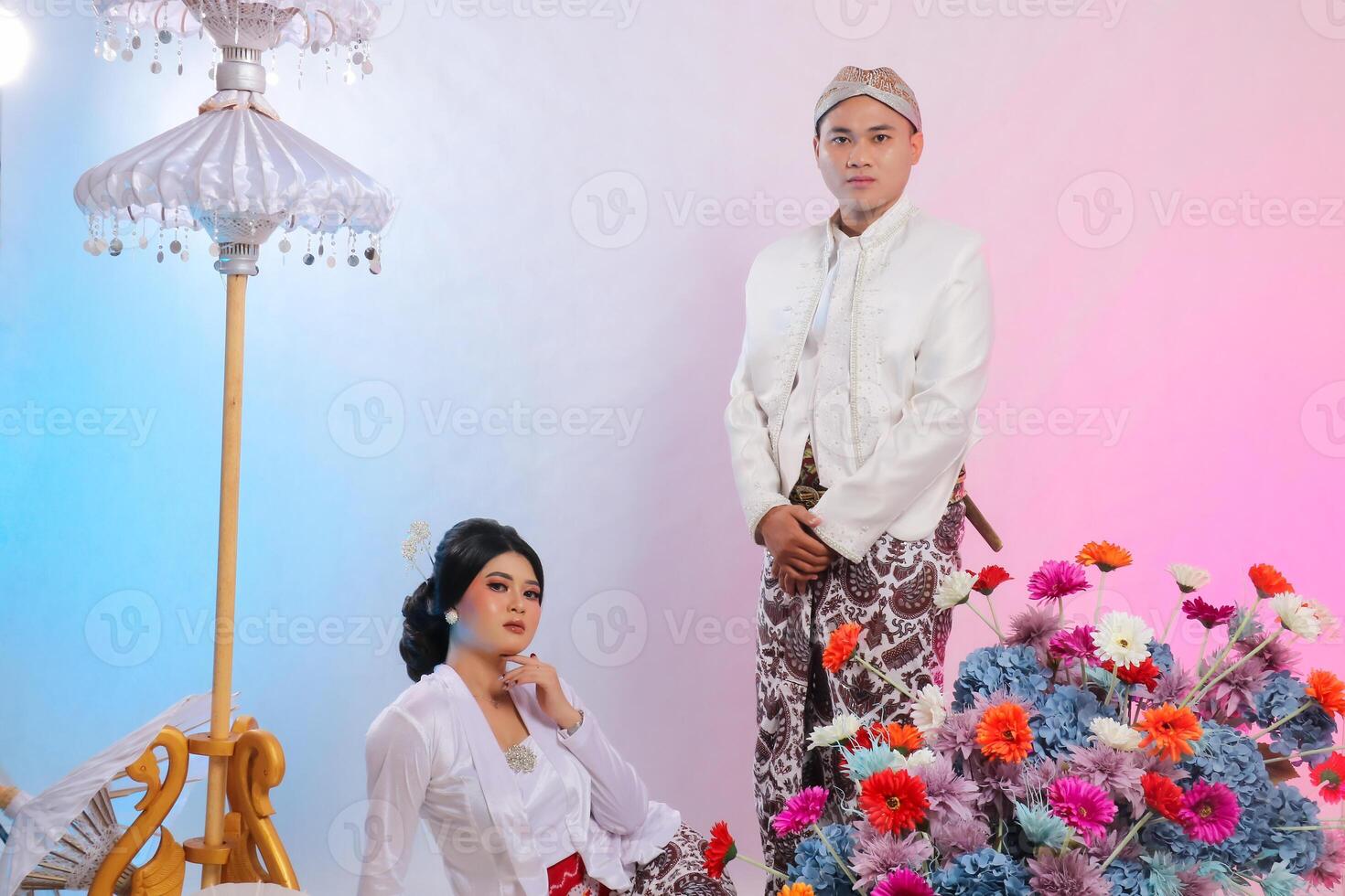 landscape of a pair of lovers, a adult indonesia boy and girl, a woman sitting on the floor, a man standing wearing modern Javanese traditional for the bride and groom on a white background photo