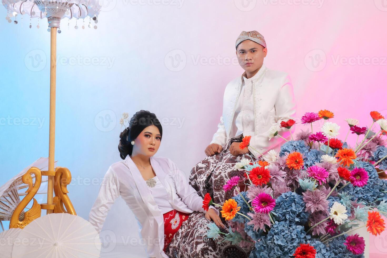 couple of lovers, indonesia man and a woman, are slumped on the floor. The man is sitting on a chair wearing modern Javanese traditional clothing, a white velvet for the bride on a white background photo
