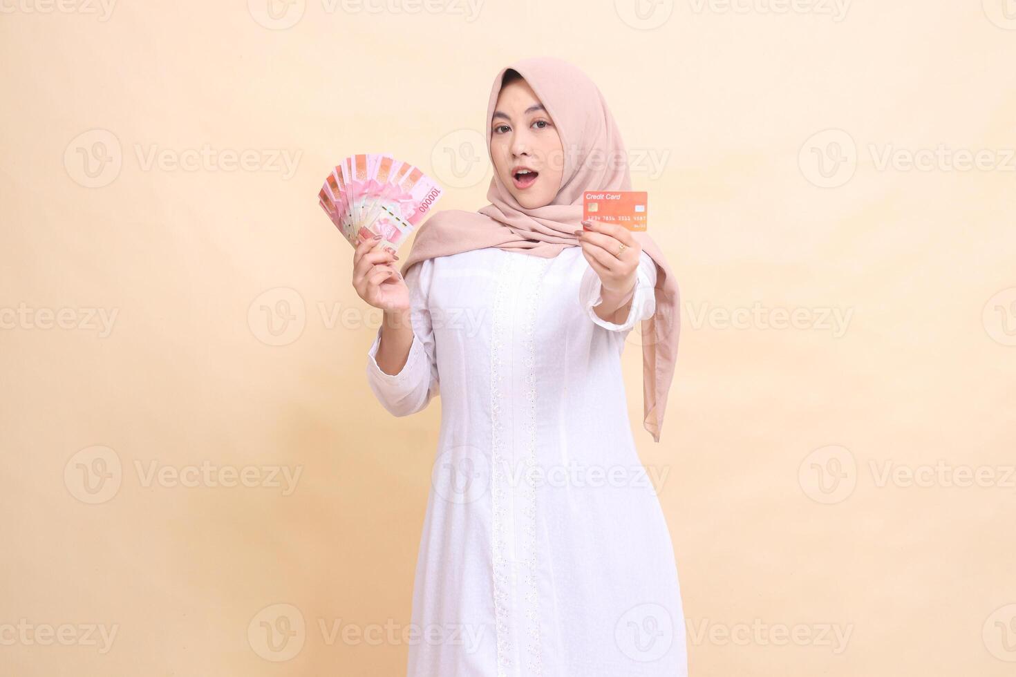 Muslim woman indonesia in hijab looks elegant holding rupiah cash and credit card in hand. Lifestyle, religious, business and finance concepts photo