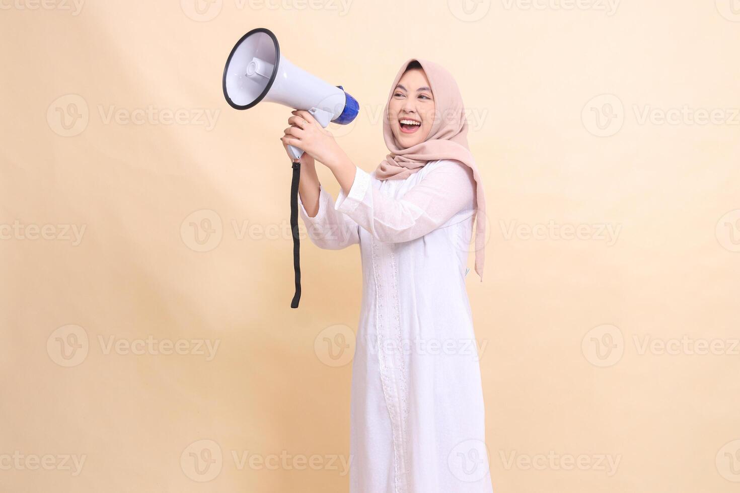 young girl asian wearing hijab slanted to the right candidly shouts cheerfully holding a loudspeaker megaphone with both hands. Technology, broadcast and promotion concept photo