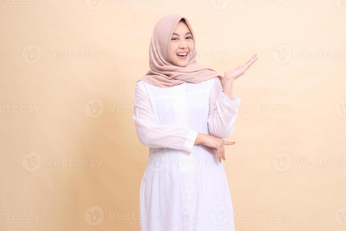 woman indonesia muslim standing to the camera cheerful smile with arms presenting to the left. Fashion, pointer, business and promotion concept photo