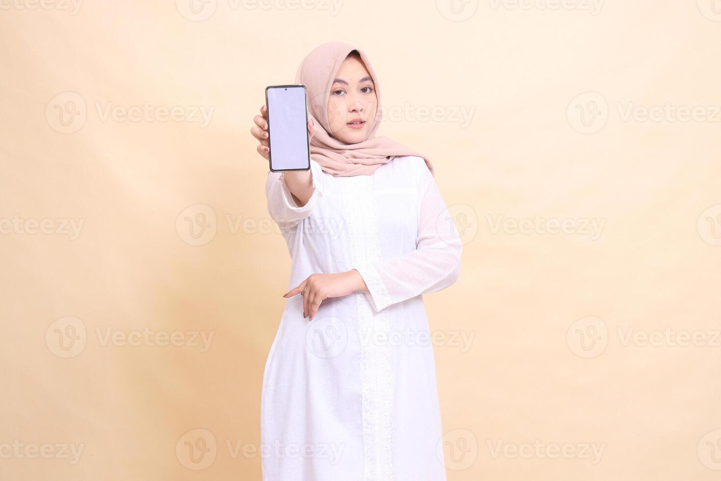 portrait of an Asian Muslim woman wearing an elegant hijab holding a cell phone gadget in her hand in front of her with her arms crossed. Lifestyle, business and finance concept photo