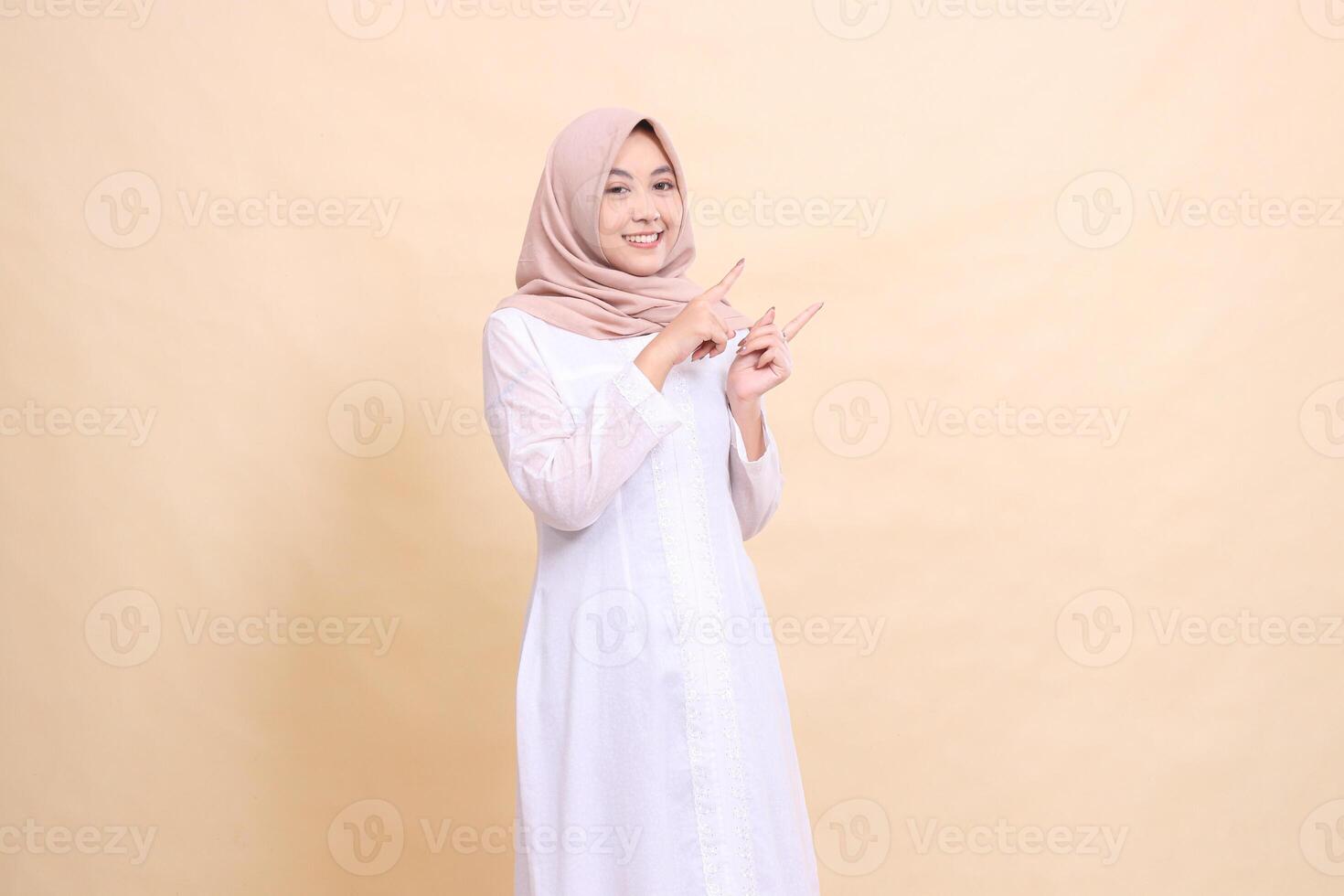 young Asian Muslim woman standing smiling both hands pointing to the top left. Fashion, pointer, business and promotion concept photo