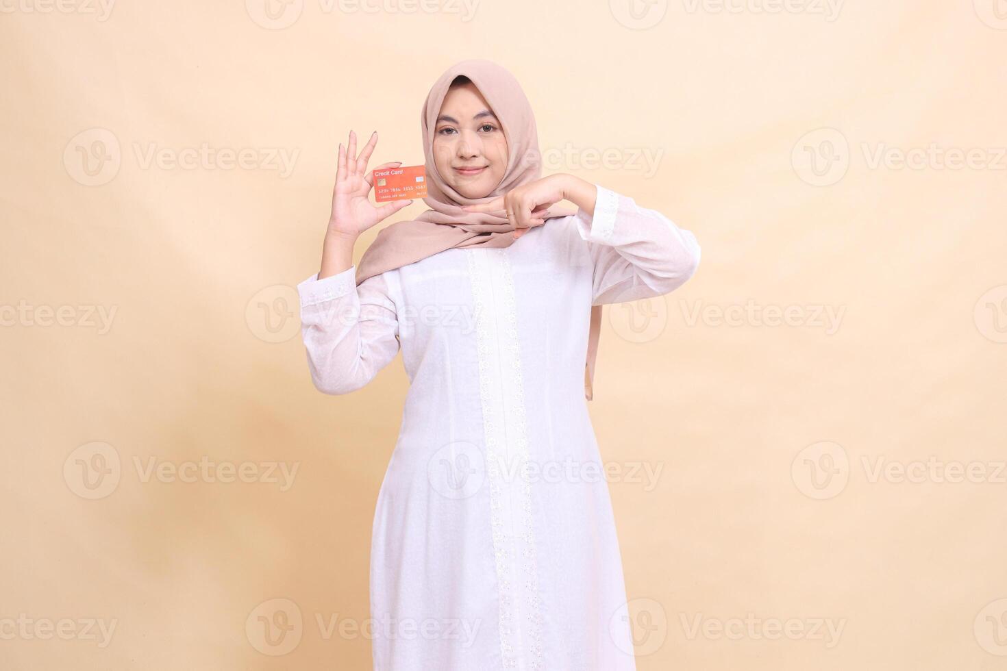 woman indonesia beautiful in hijab smiles holding debit credit card in her hand and pointing at it. Lifestyle, business and finance concept photo