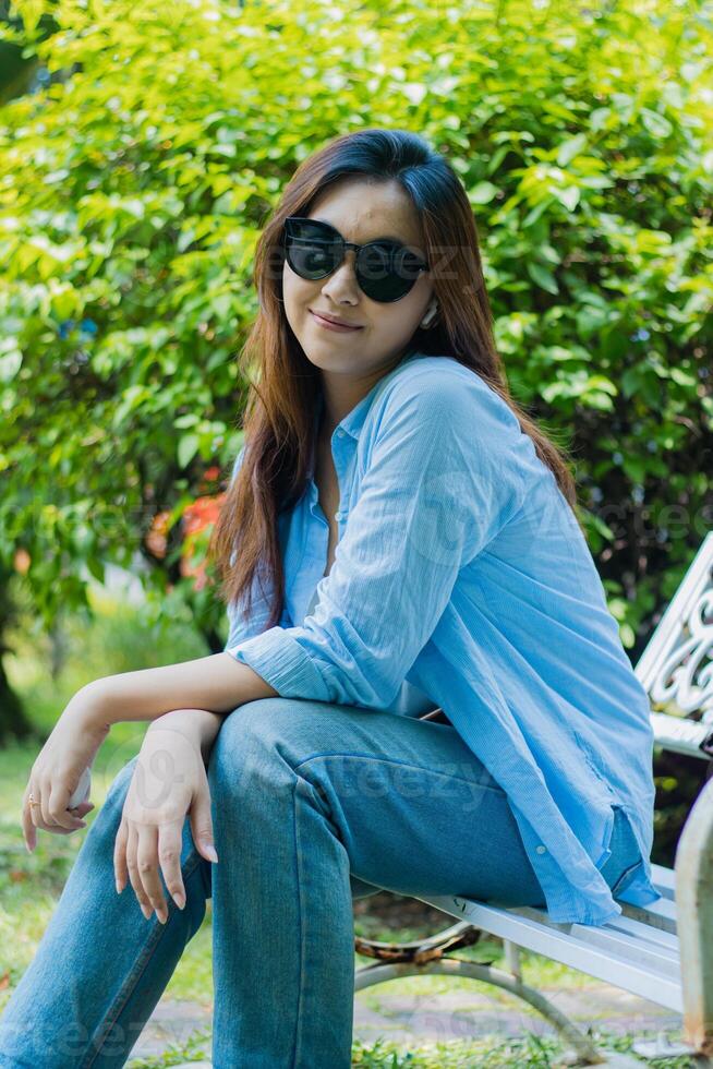 portrait Asian mature woman in glasses looking at camera smiling sitting in outdoor park. female students for the themes of education, technology and advertising photo