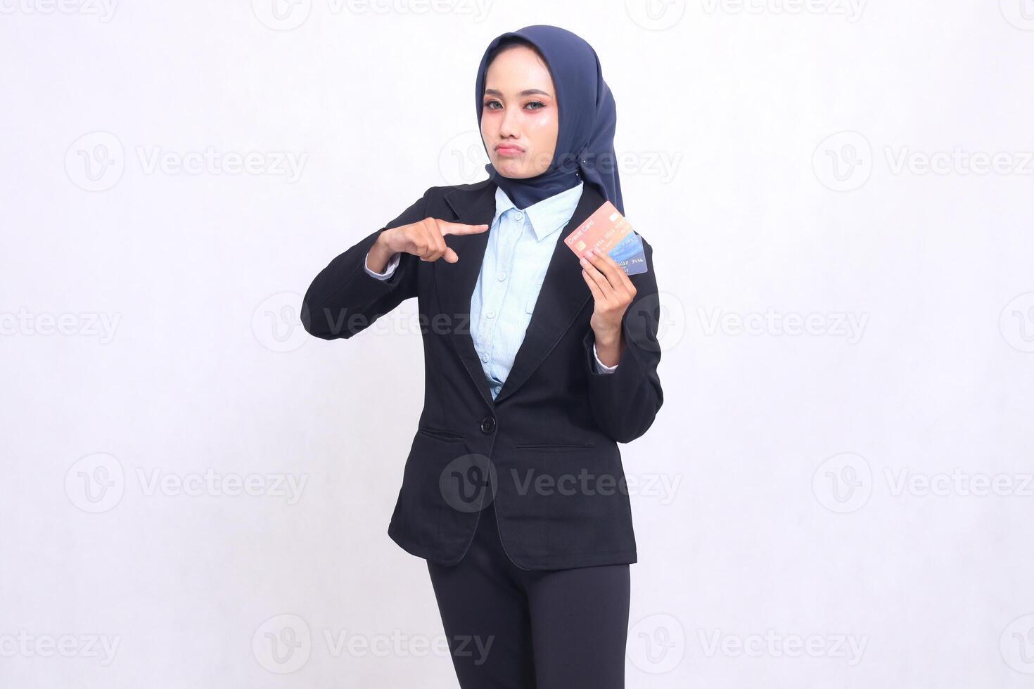 Mature Asian office woman wearing a hijab stands sullenly pointing and carrying a credit debit card for ease of making a bank savings book. adult Muslim blue shirt for finances, transactions and loans photo