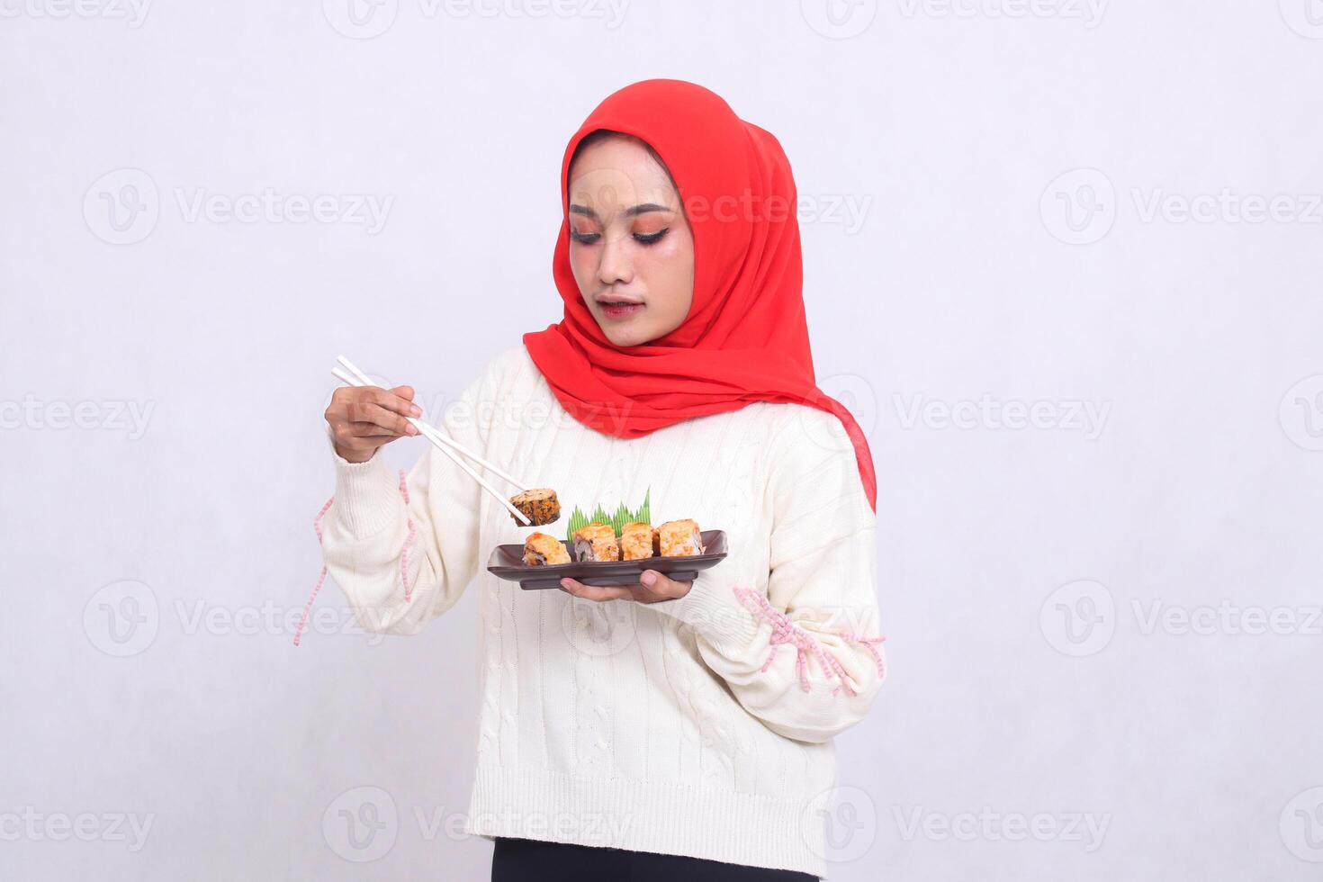 indonesia woman wearing a hijab slanted to the right takes chopsticks and carries a plate containing sushi Japanese food. Beautiful Muslim women are used for culinary, food and advertising content photo