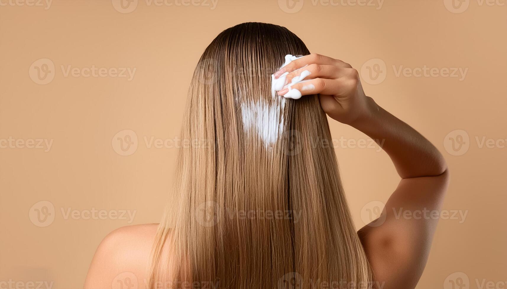 Young woman applying hair mask on beige background, back view photo