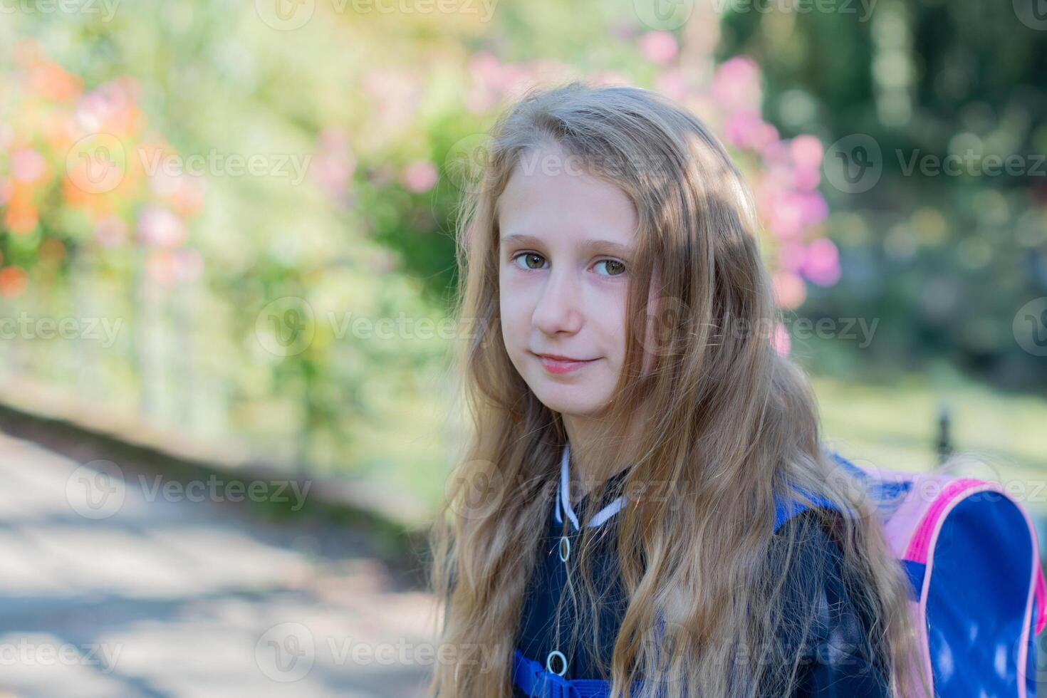 Back to school, portrait of a little girl from primary school outdoors, enjoying flowers in a flowerbed and looking at the camera with a smile, student dressed in dark blue uniform photo