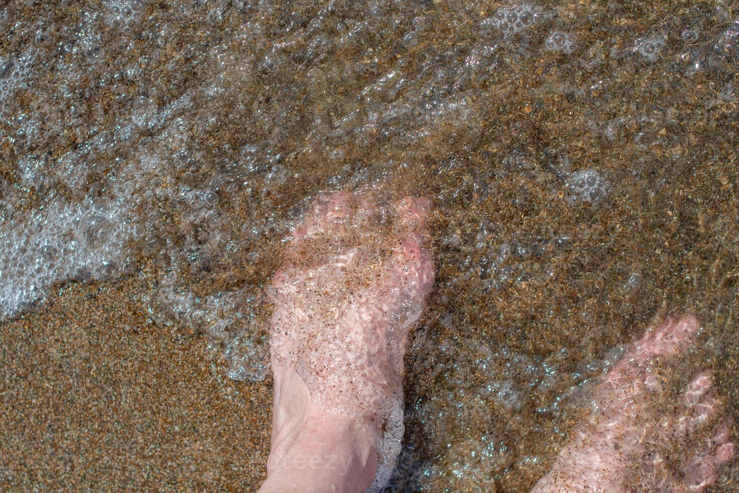 hembra pies descalzo en olas de espumoso agua en un arenoso playa en un verano día, parte superior ver de hembra pies, mujer en el playa consiguiendo su pies mojado en calentar mar agua, despreocupado vacaciones por el mar, foto