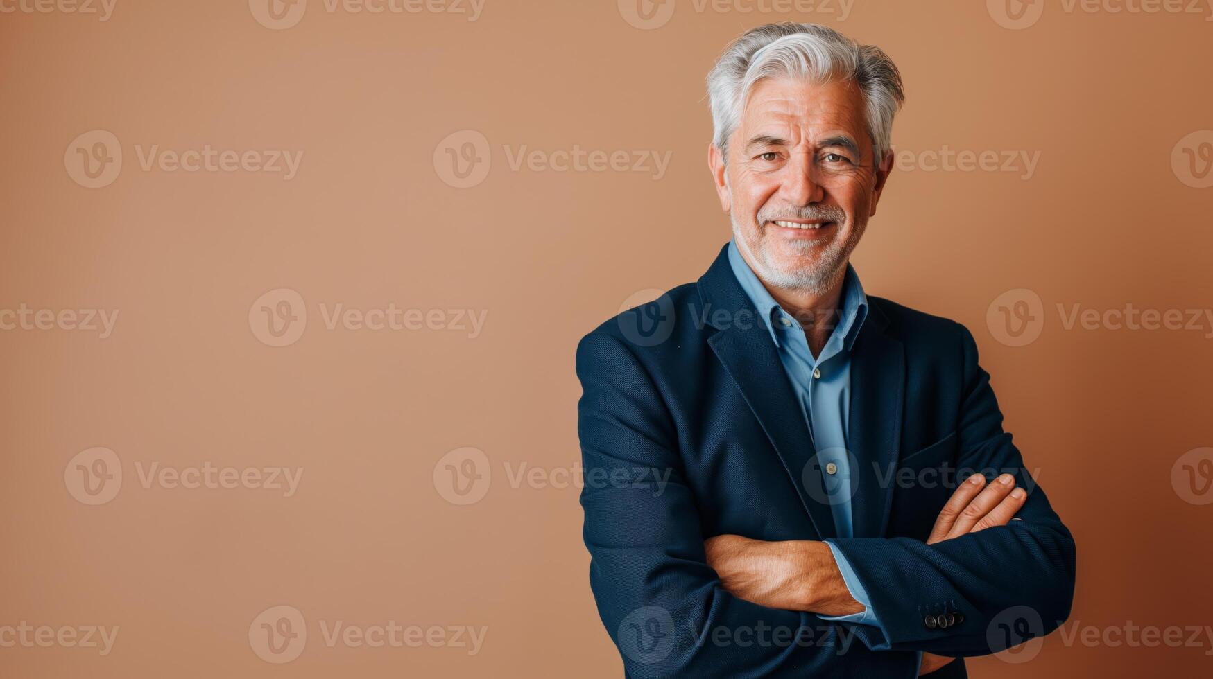 Confident Elderly Southern European Businessman in Blue Suit Standing with Arms Crossed on Brown Background photo