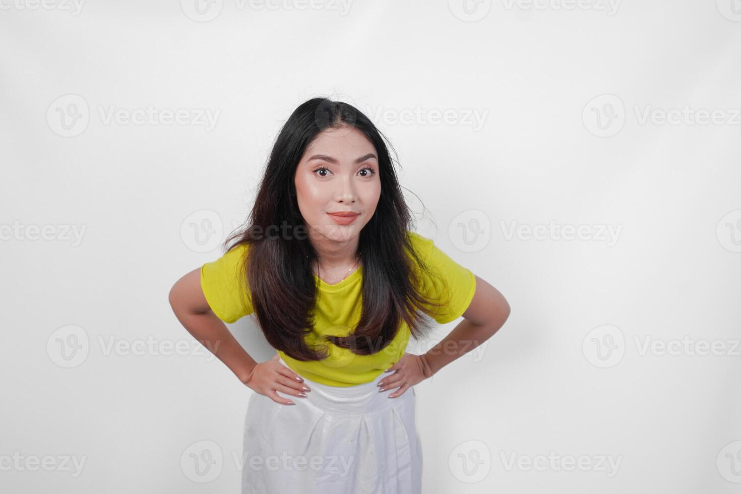 Cheerful woman in a yellow shirt and white skirt is smiling and posing for a picture with hands on hip, isolated by white background. photo