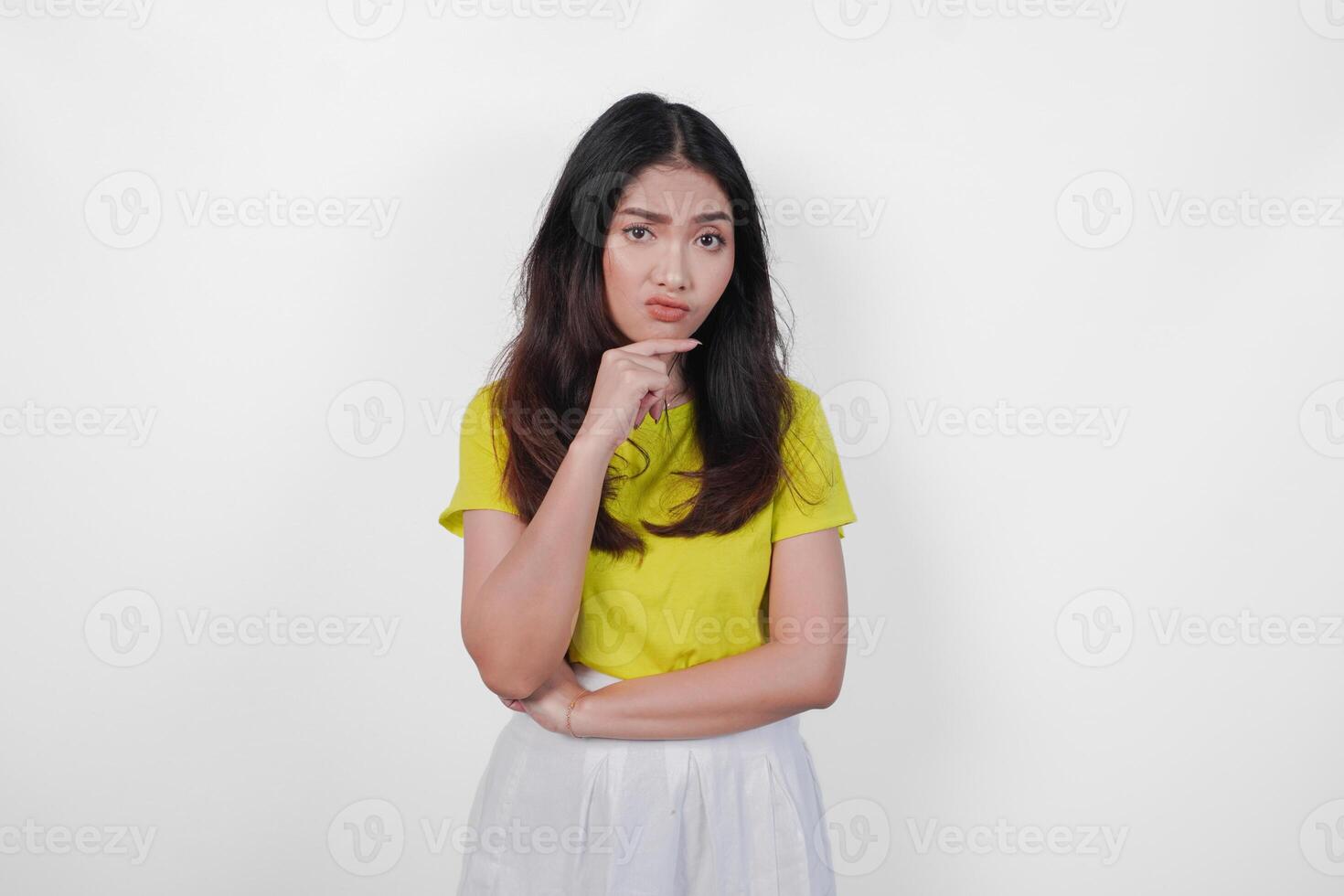 Thoughtful young Asian woman in a yellow shirt and white skirt is looking down and appears to be thinking. Concept of introspection and contemplation. photo